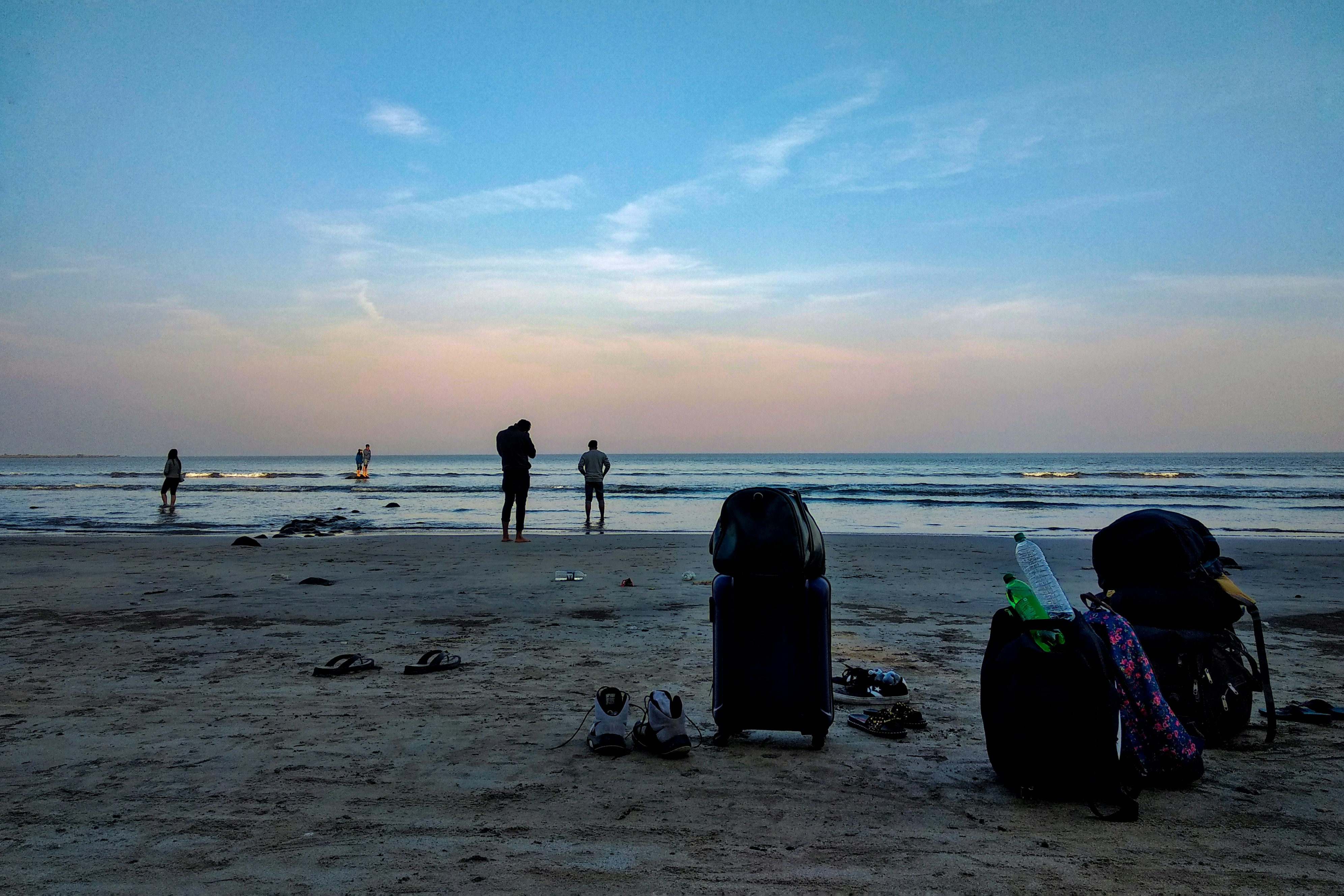 Two people paddle in the shallows at Mandwa Beach, near Mumbai. The pair's belongings, including a bag and some shoes, sit on the sand in the foreground.