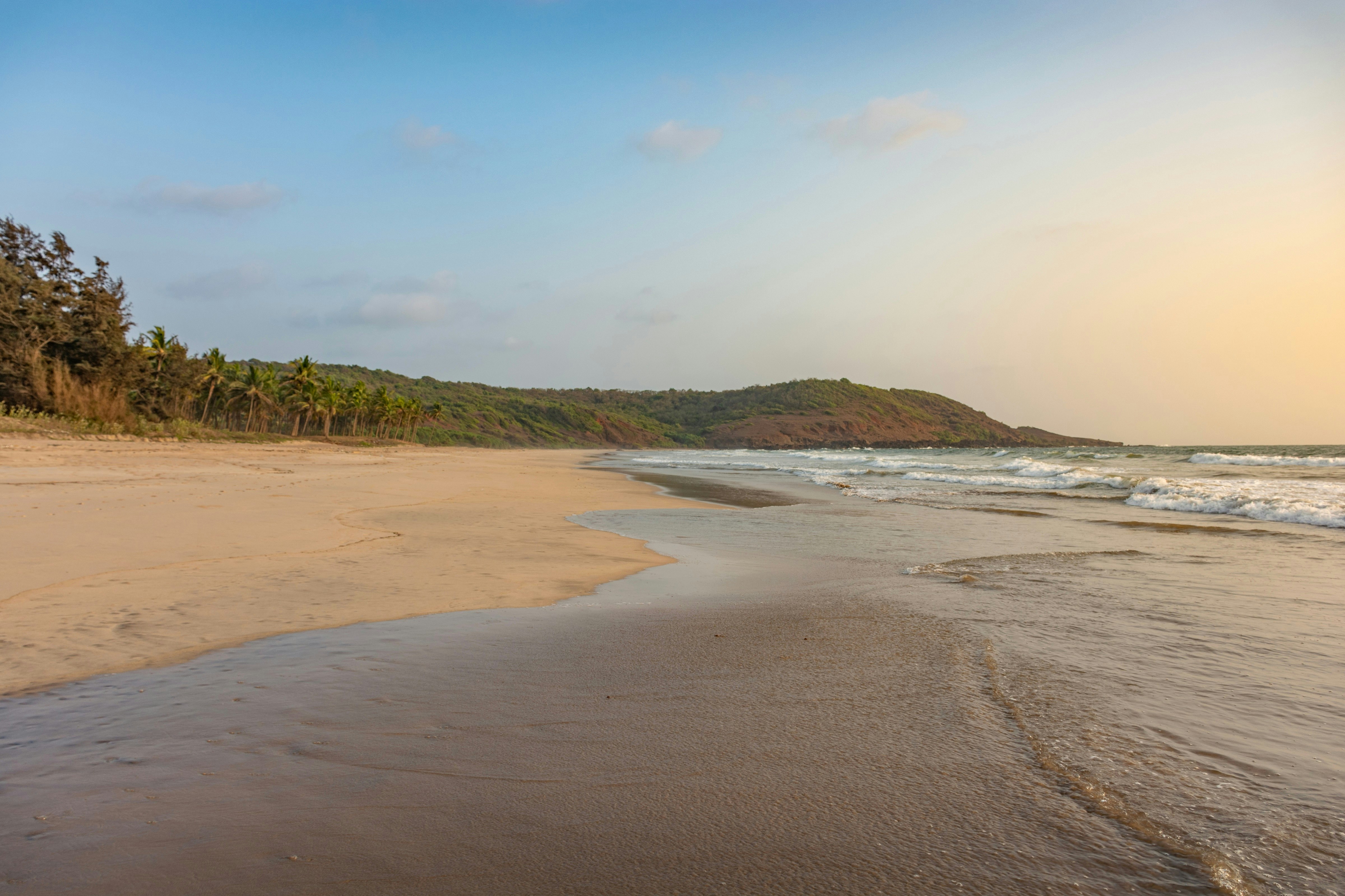 The golden sands of Ganpatipule beach. The waves lap the shoreline, which is completely empty and backed by forest.