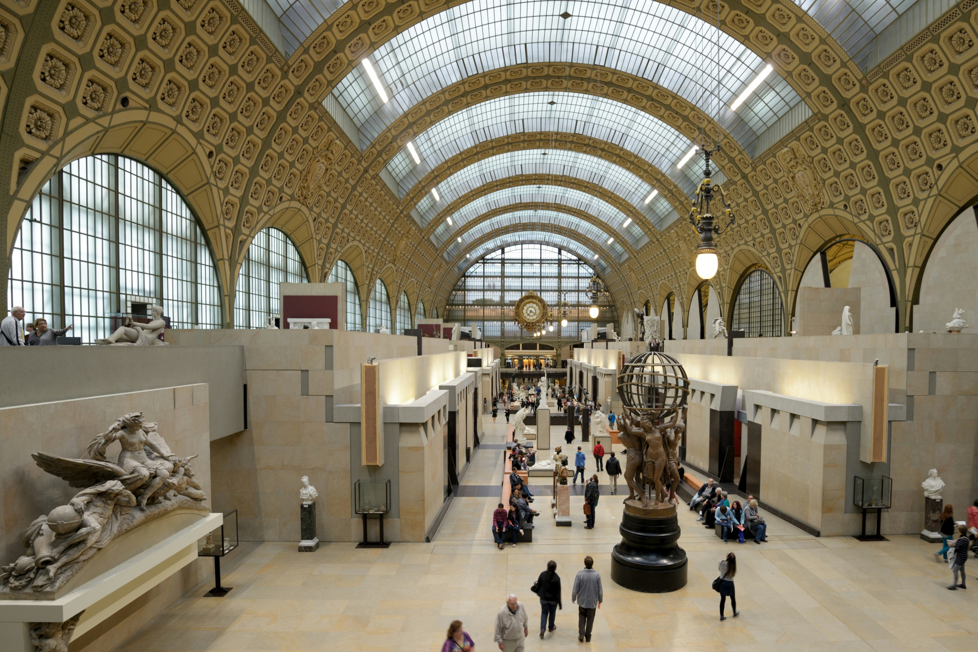 Den storslagna, rymliga interiören av Musée d'Orsay i Paris med många människor som promenerar runt utställningarna som inkluderar stora statyer och målningar