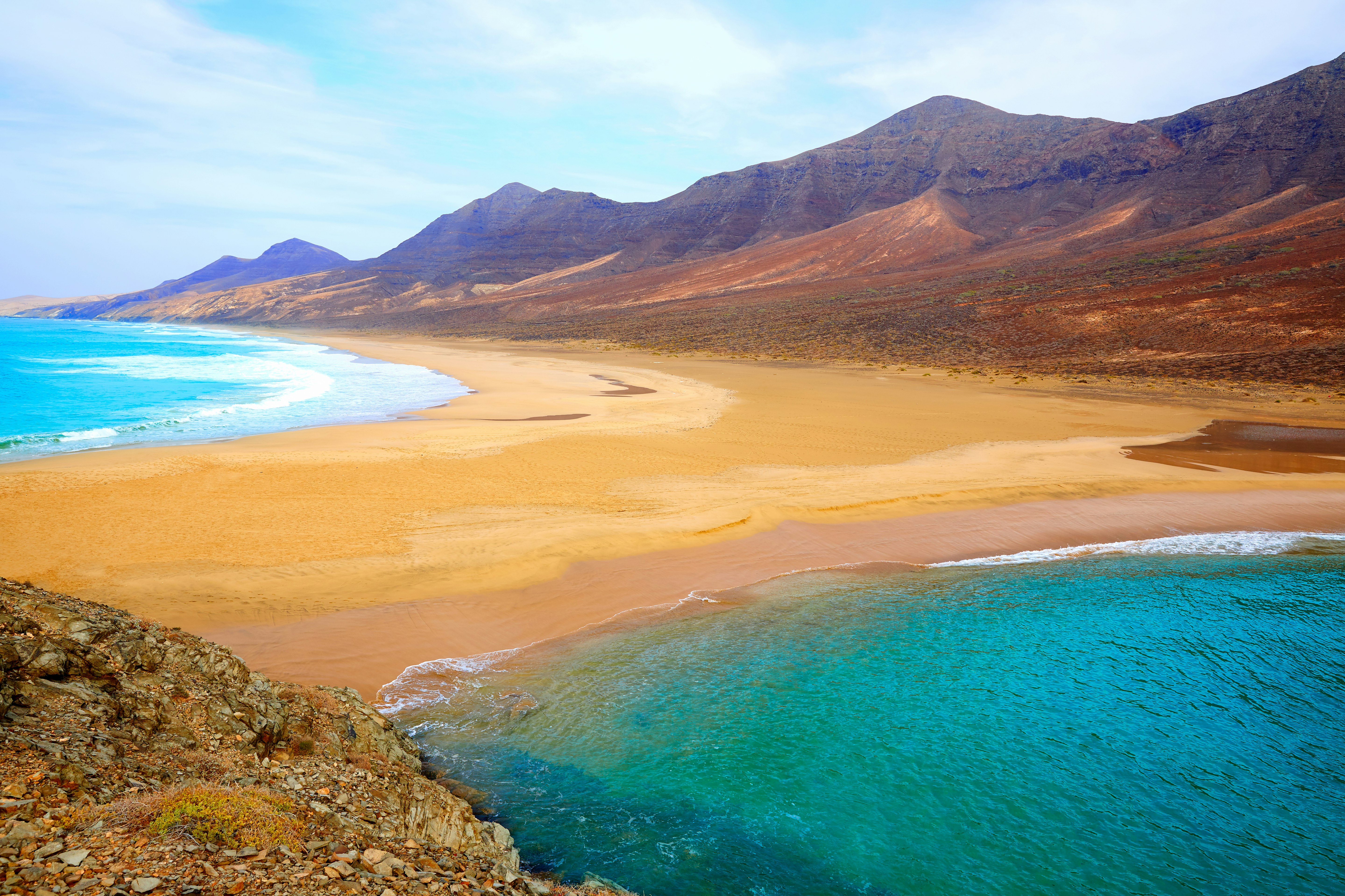 A golden stretch of sand is lapped on either side by azure water on Fuerteventura, Canary Islands