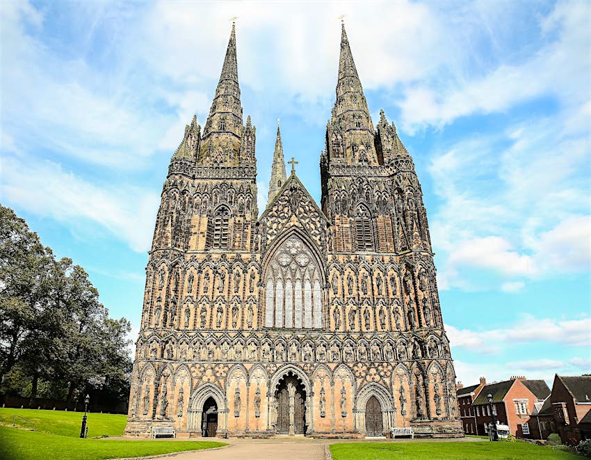 obturador_482774215.jpg Mirando hacia arriba a la elaborada fachada gótica de una catedral de piedra de tres agujas cubierta de estatuas.