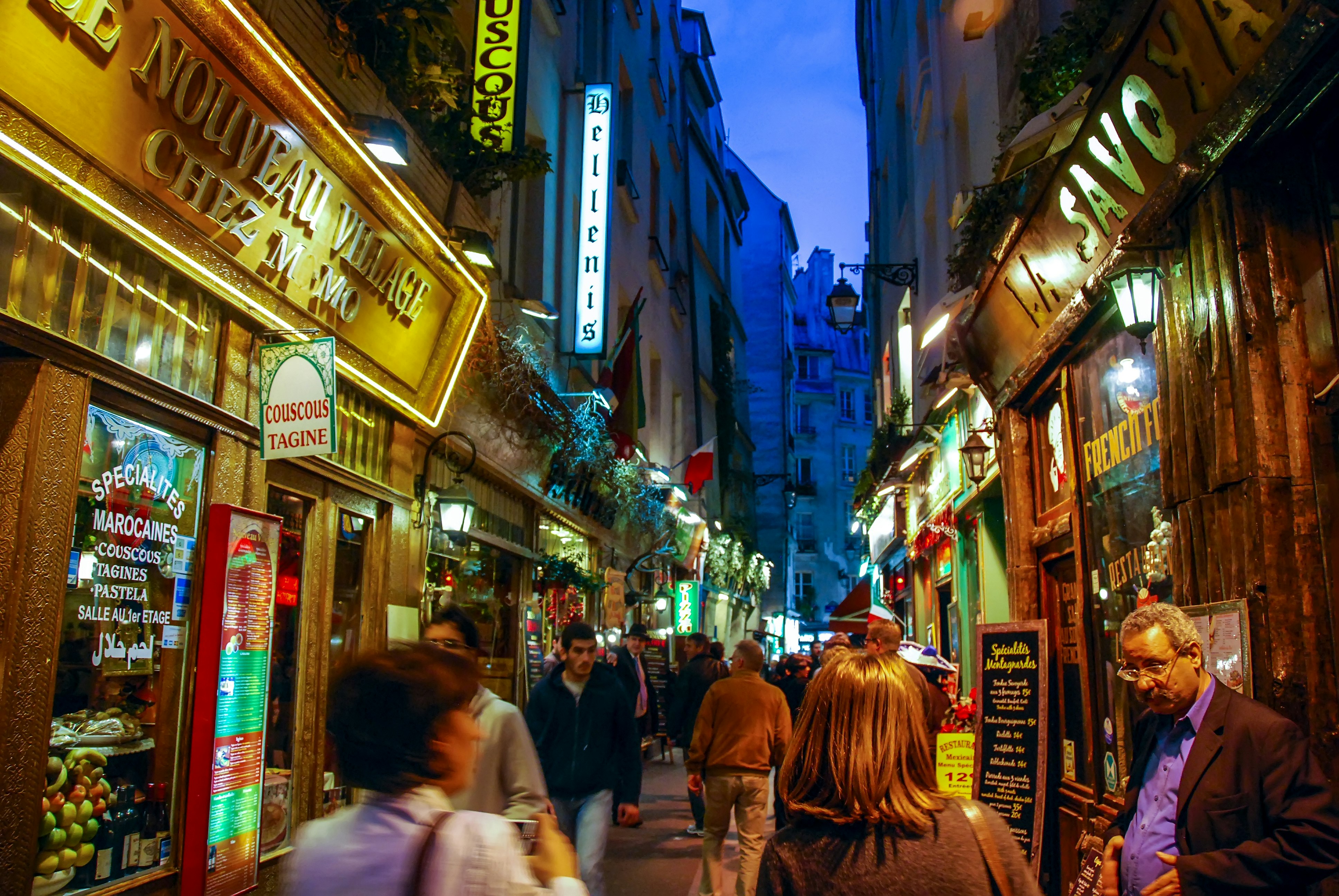 A busy street in Paris' Latin Quarter at night, with bars and restaurants lining the street all lit up