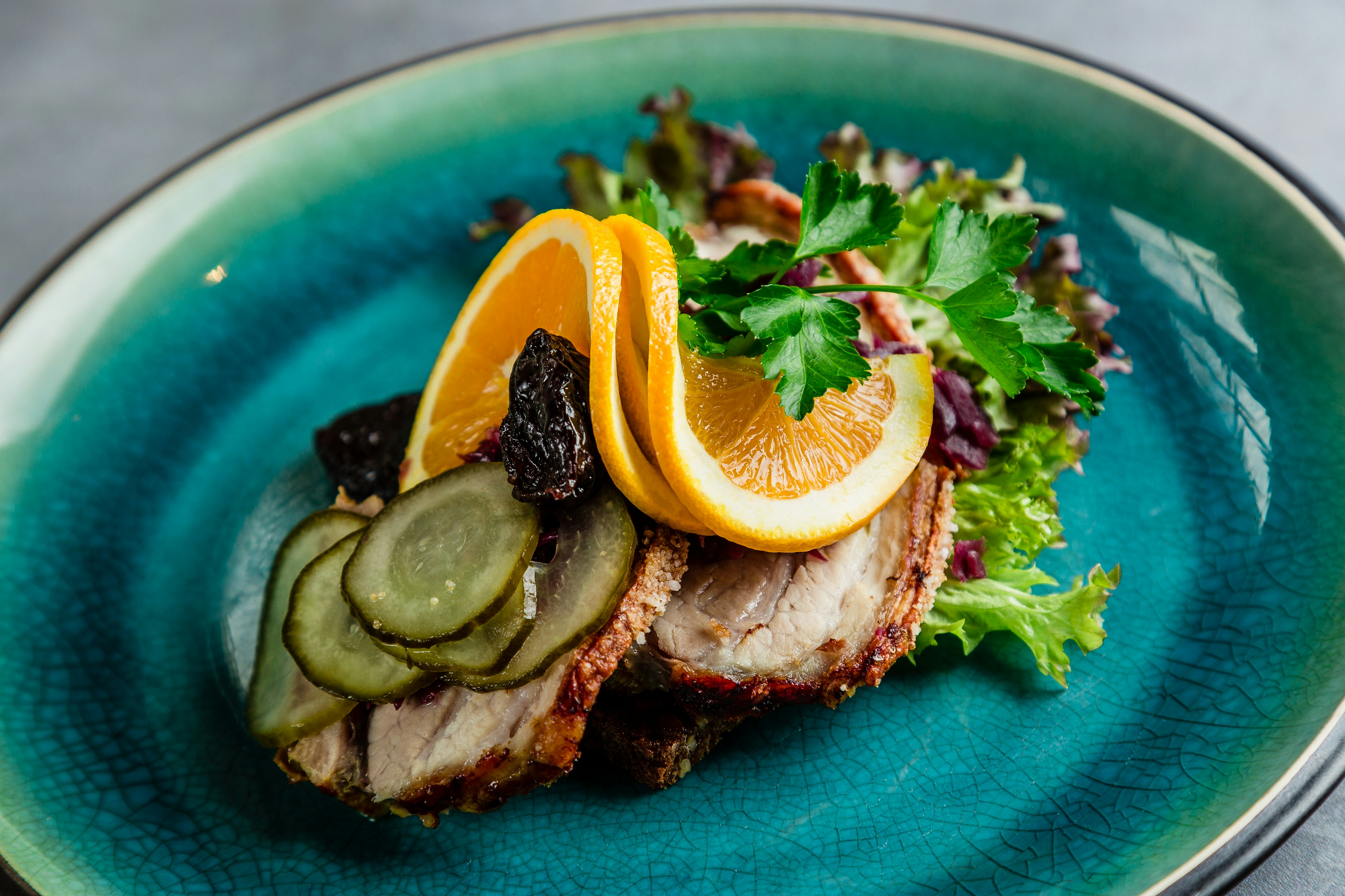 A slice of bread topped with meat, cucumbers, dried fruit, lettuce and orange slices