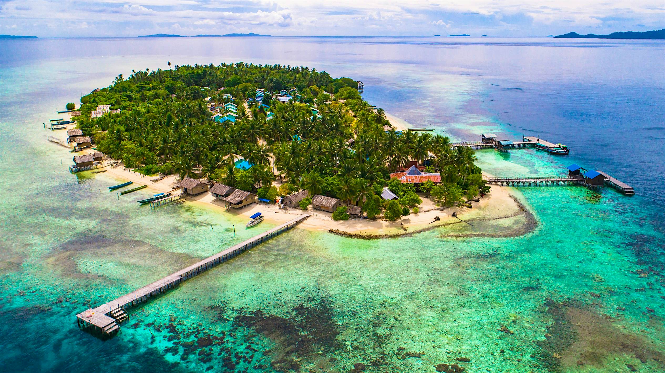 Arborek island, Indonesia An aerial view of the island of Arborek island, a small island in Indonesia's Raja Ampat archipelago. The island is ringed by a ribbon of light blue waters and a coral reef beneath the surface.