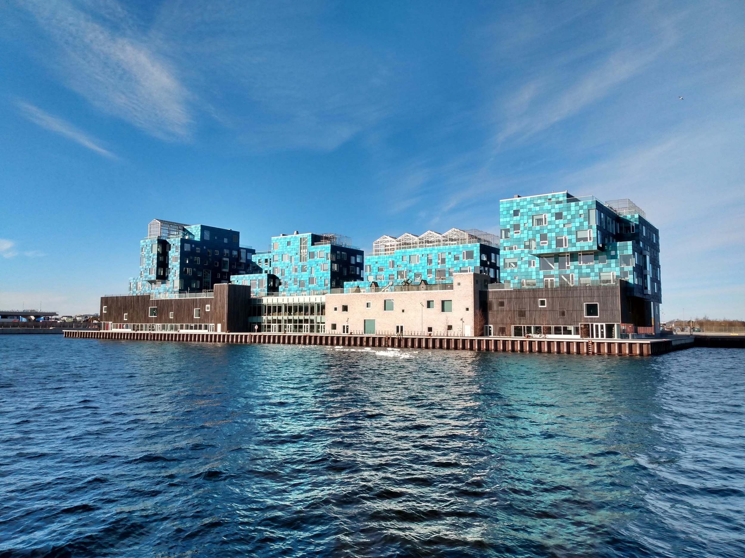 A large building on the edge of the water, covered in bright blue tiles that act as solar panels.