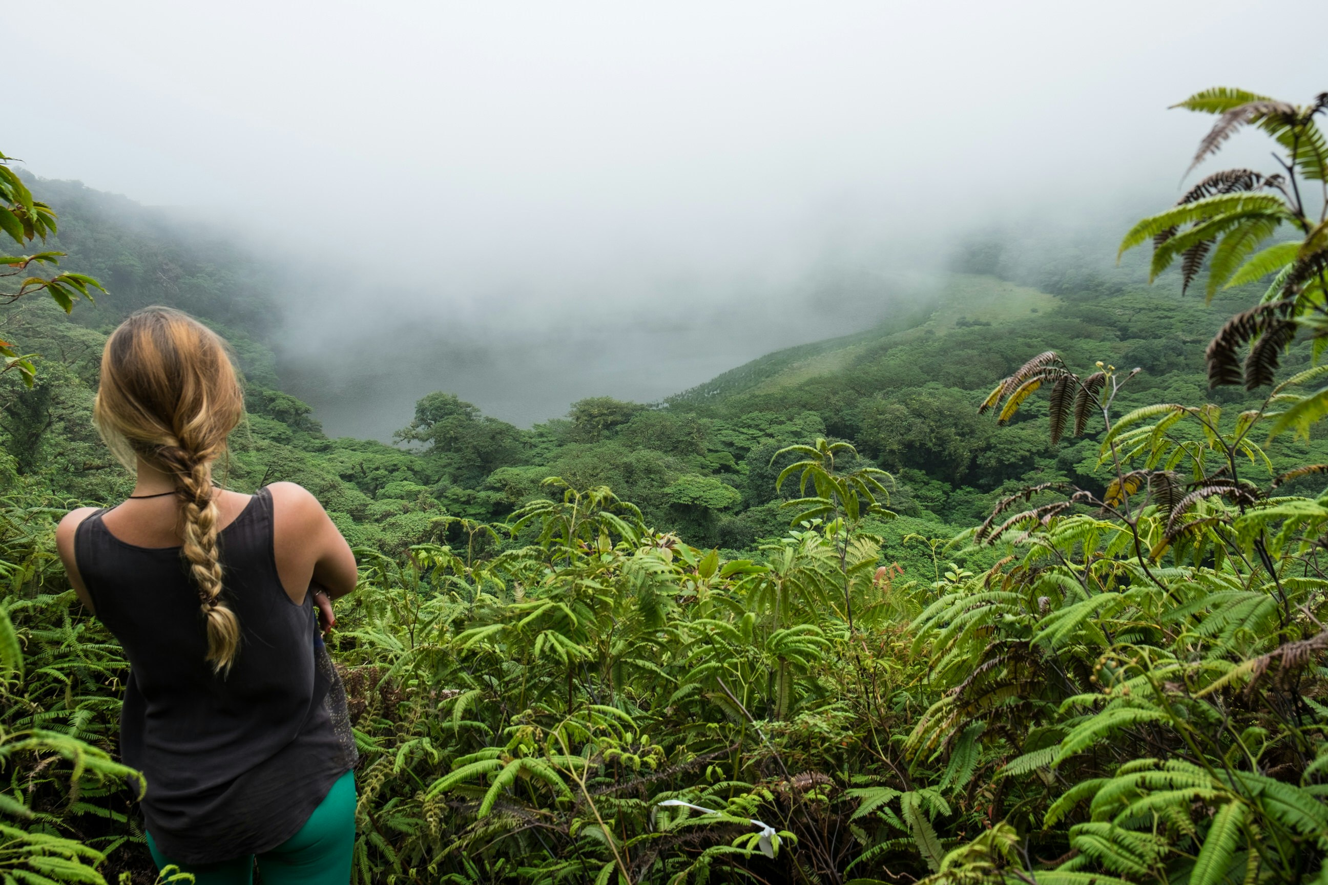 A woman looks down into the jungles below from a perch on the top of Maderas Volcano, Ometepe Island, Nicaragua
