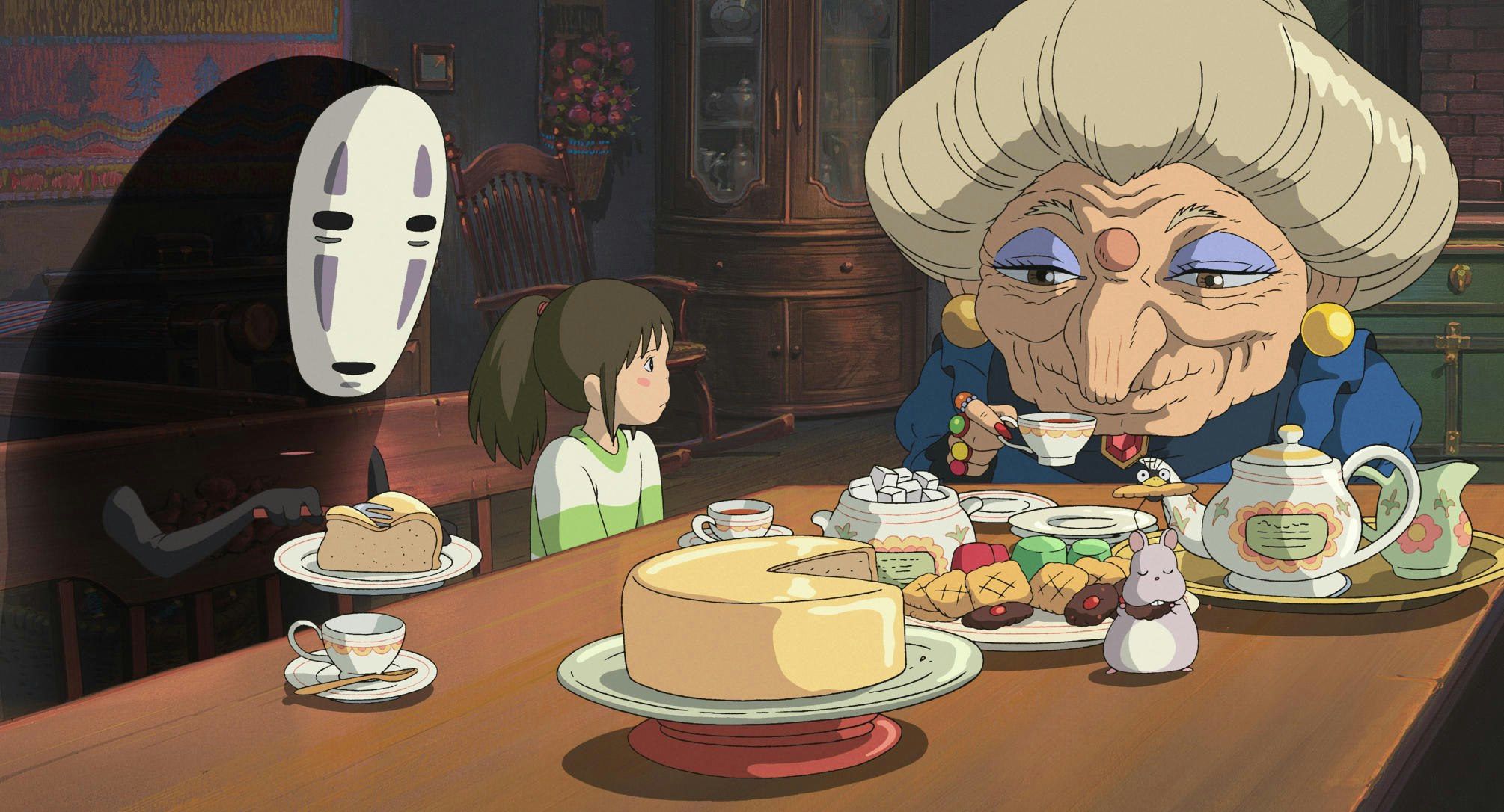 A scene from the anime movie 'Spirited Away'; young girl Chihiro is sitting at a table having tea and cake with two magical characters.