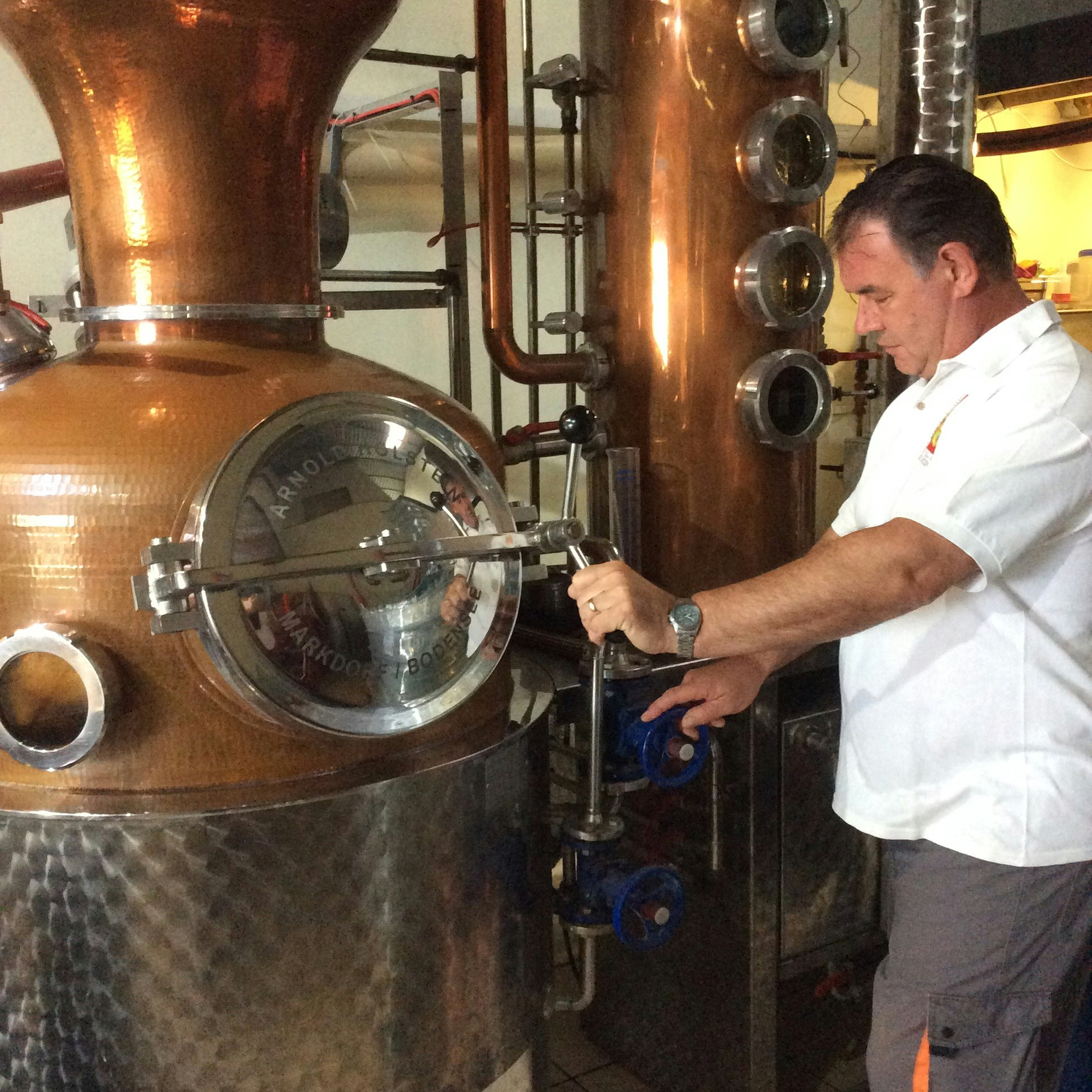 Paul Hickling standing in front of large brass distillery equipment.