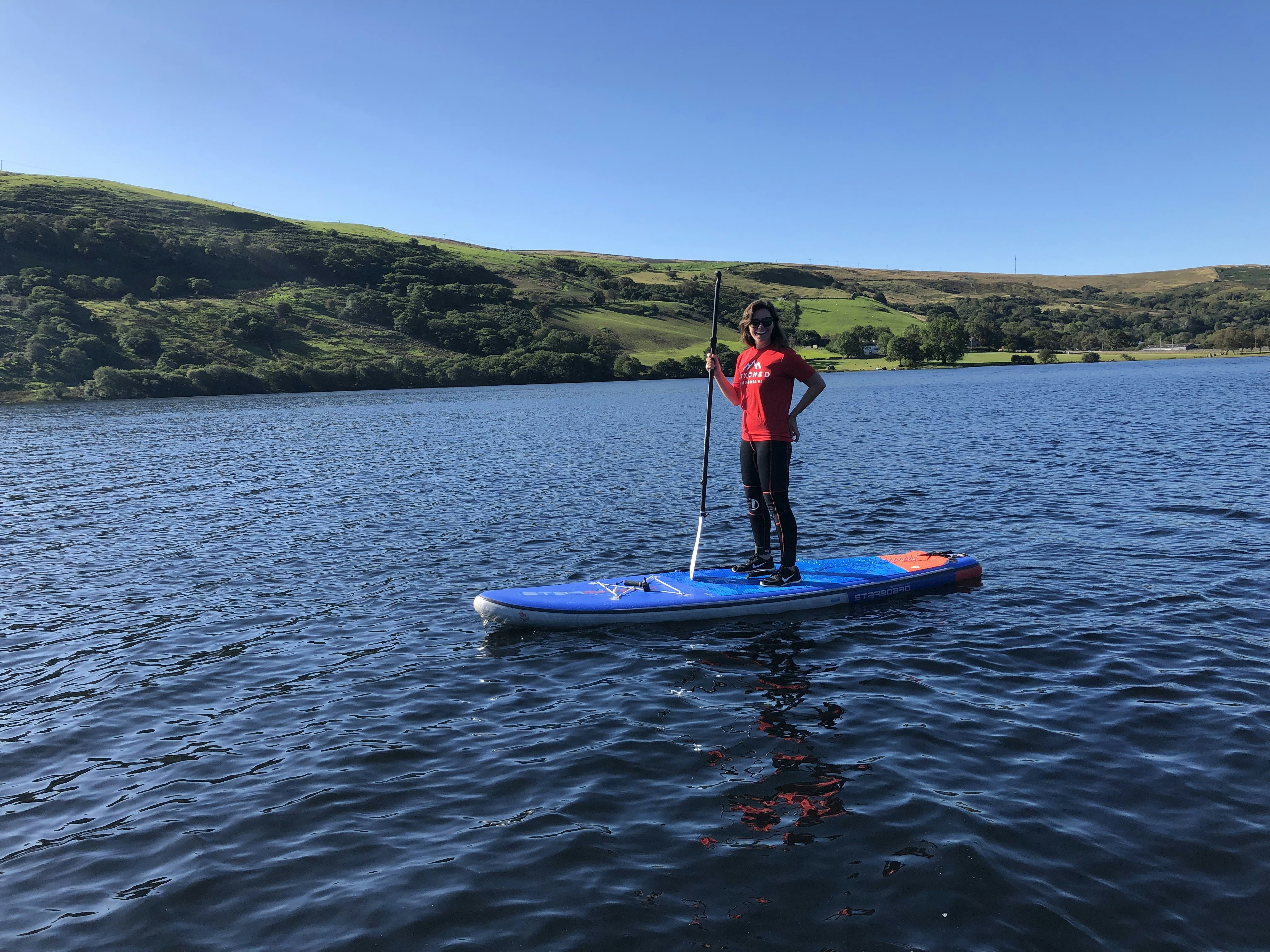 A woman stand up paddleboarding in Wales.