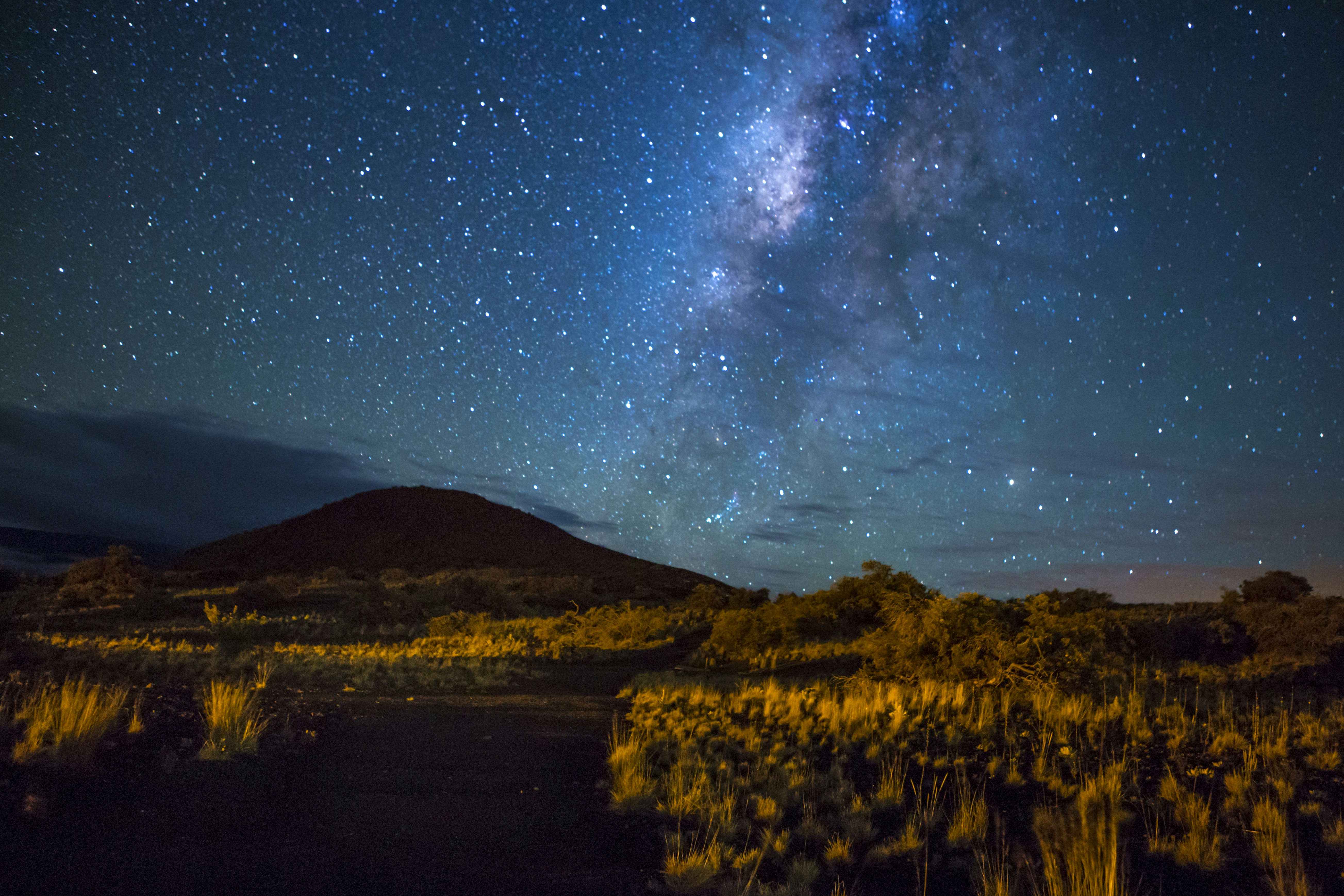 The Milky Way appears in the sky over the Hawaiian landscape, with Mauna Kea's shadow in the background