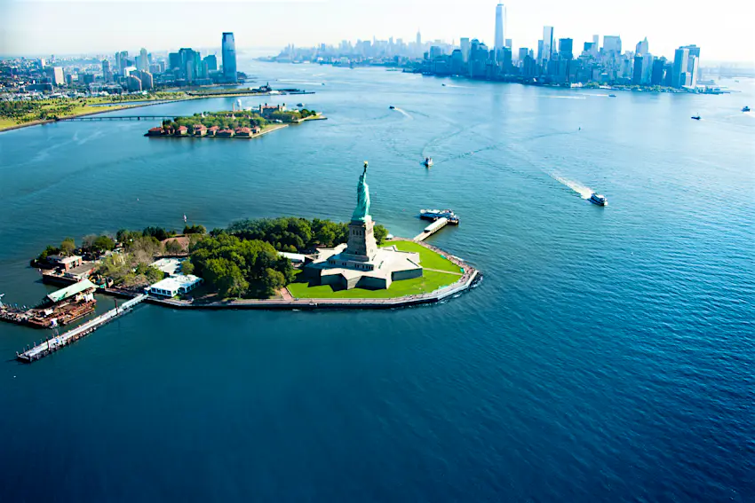 Statue of Liberty An aerial view of a statue on an island with a city skyline behind