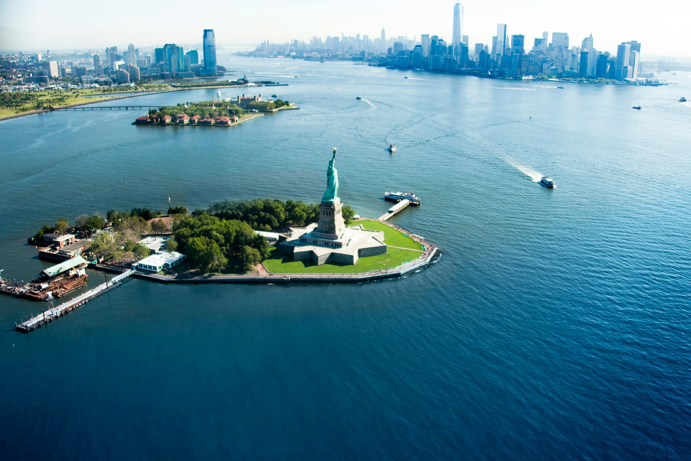 An aerial view of a statue on an island with a city skyline behind