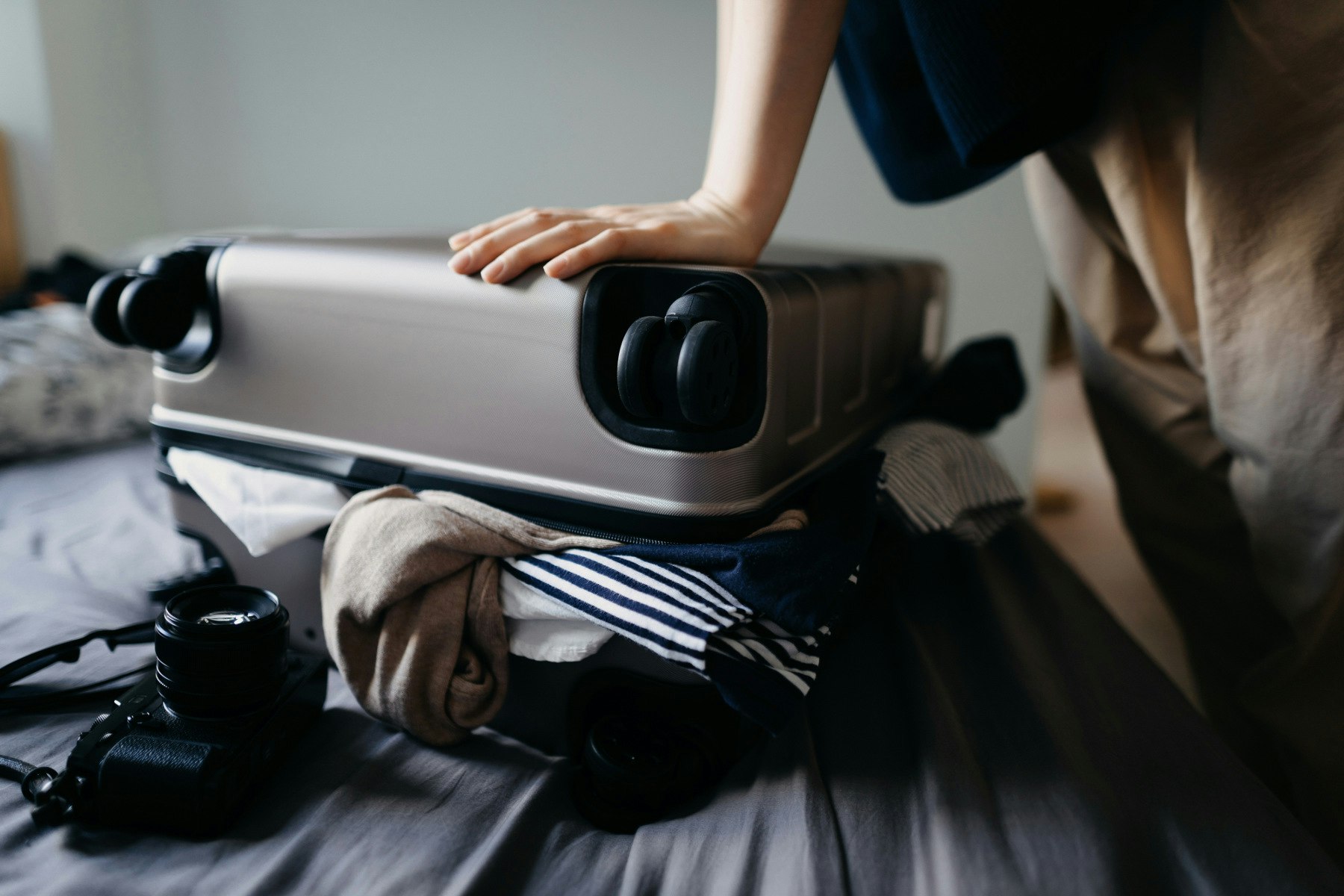 Woman struggling with overflowing suitcase on the bed at home