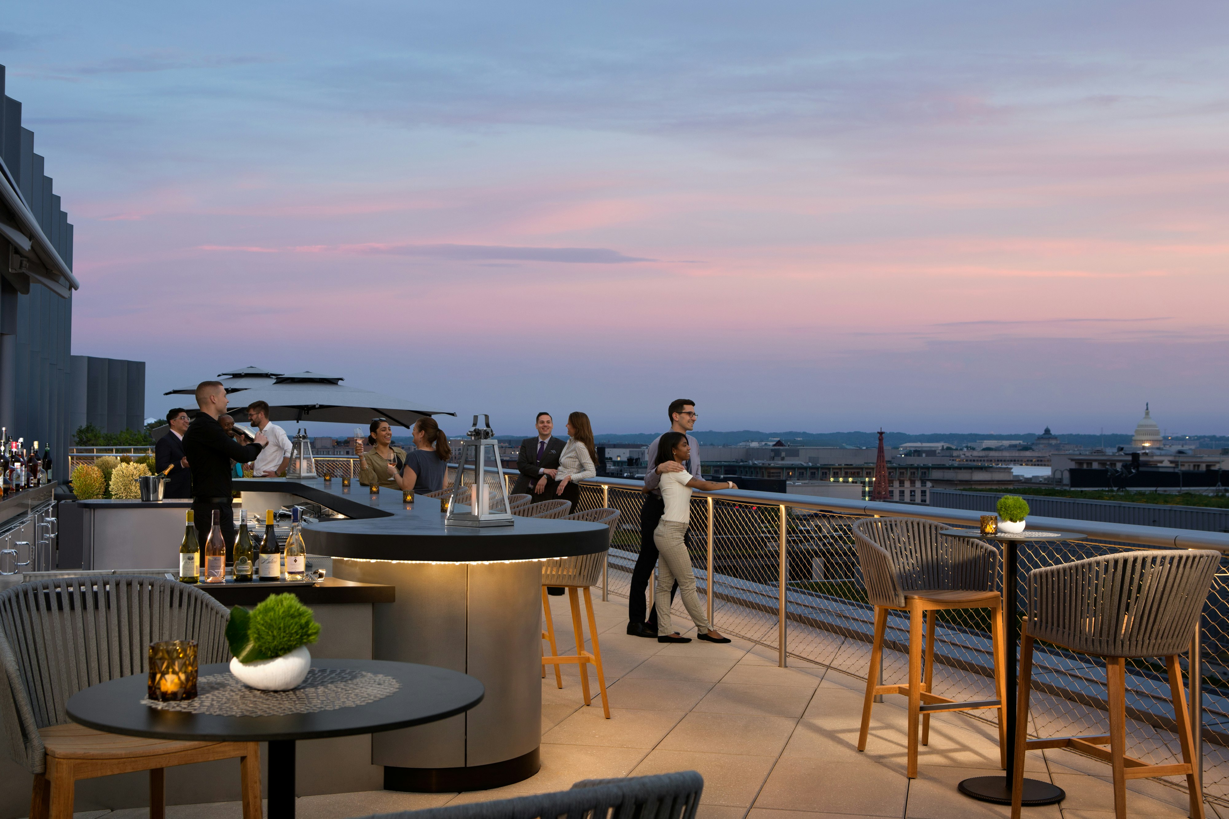 A bartender is shaking a cocktail while a group of people take in the views towards the US Capitol building at Summit rooftop bar.