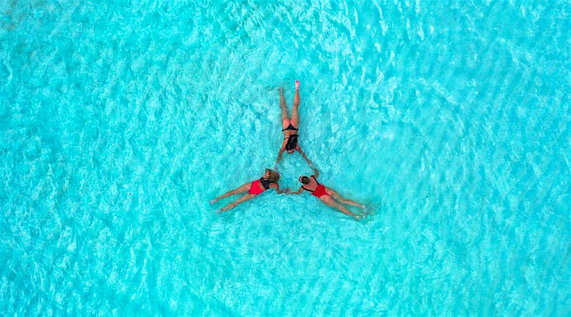 Looking down on three women floating in a rippling swimming pool on their fronts, holding hands in a ring.