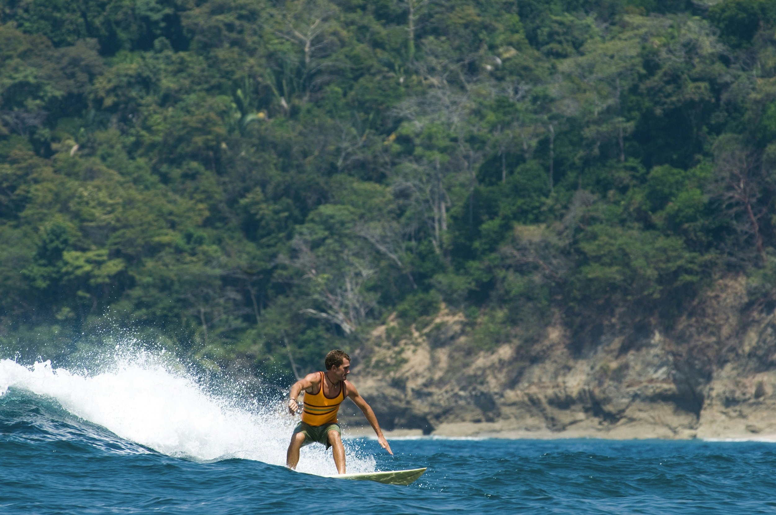  young man surfing a wave on the coast of Dominical; he's riding left to right, with the tree covered rocky cliffs in the background