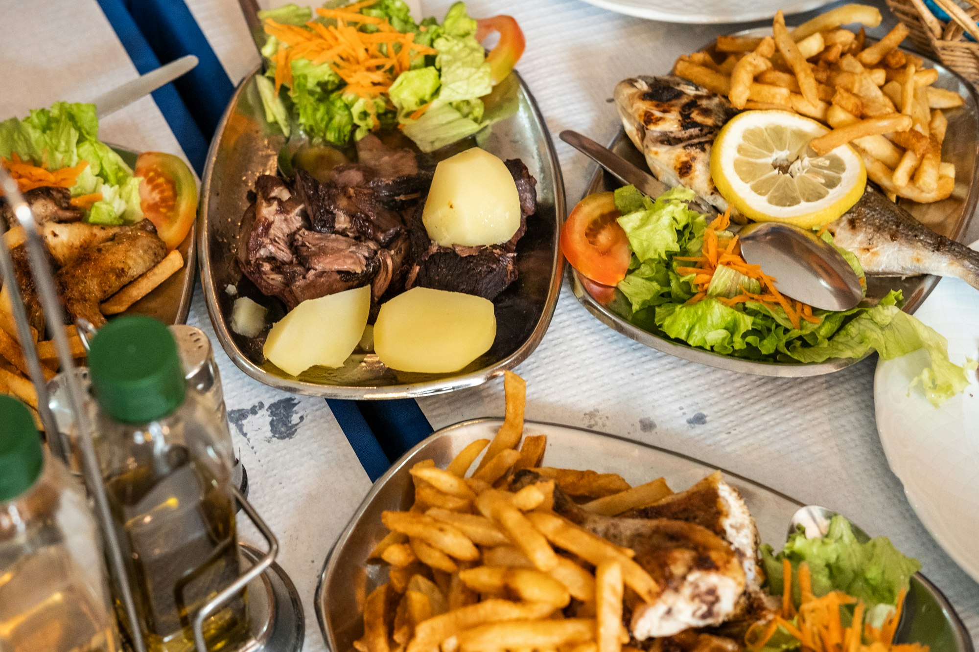 A table is laid with metal dishes containing a variety foods, from barbecued meat, to chips and salad.