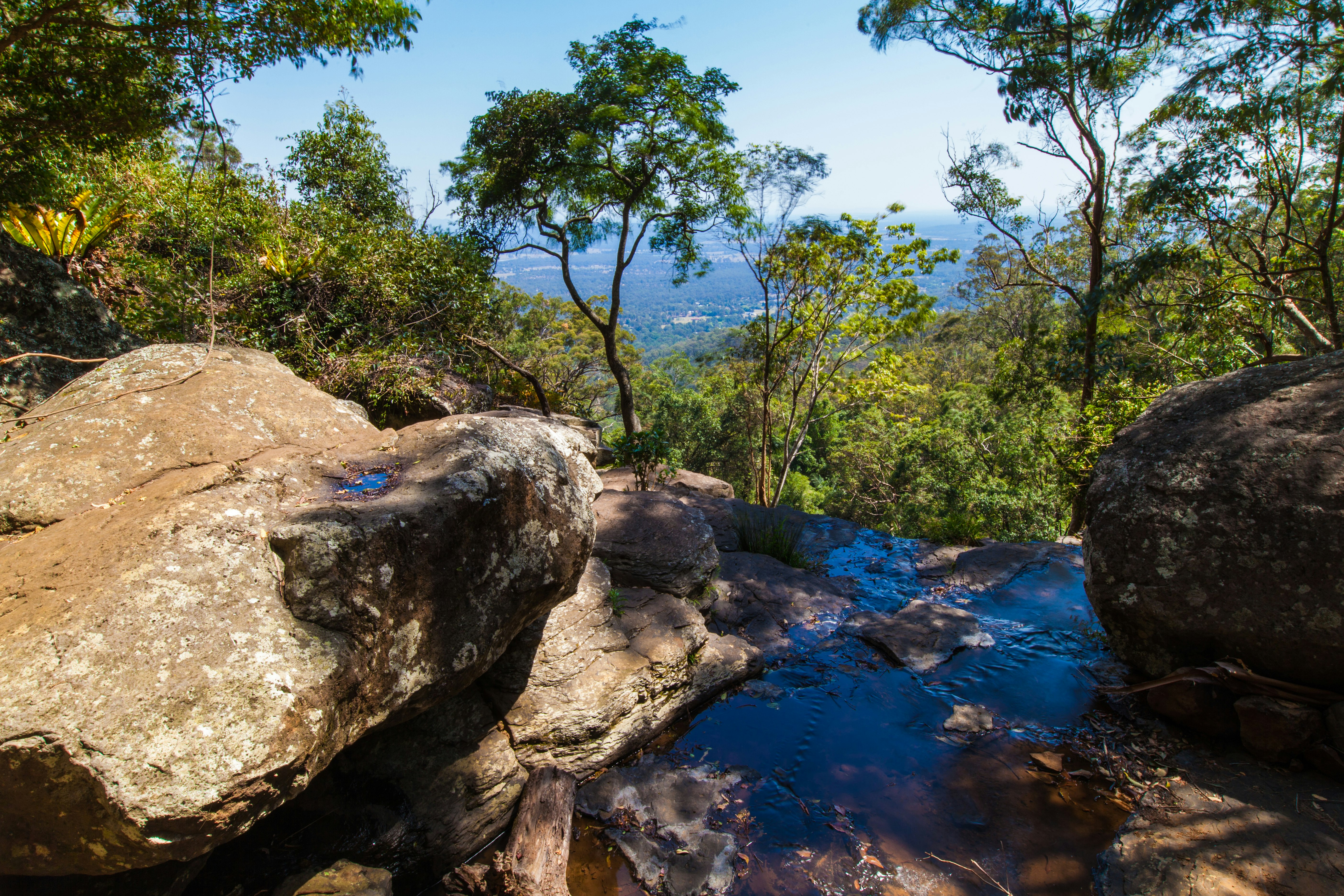 A shallow pool surrounded by large rocks on Tamborine Mountain, looking out over an expanse of rainforest.