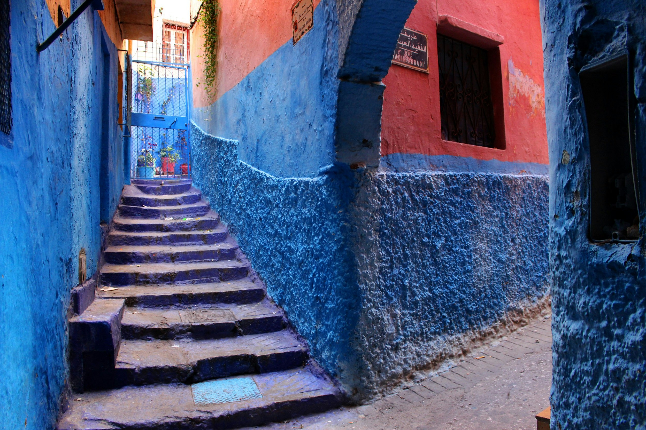 This images looks up some empty steps in an atmospheric alley in Tangiers; the lower walls are a bright blue, while the upper sections are a vibrant salmon colour.