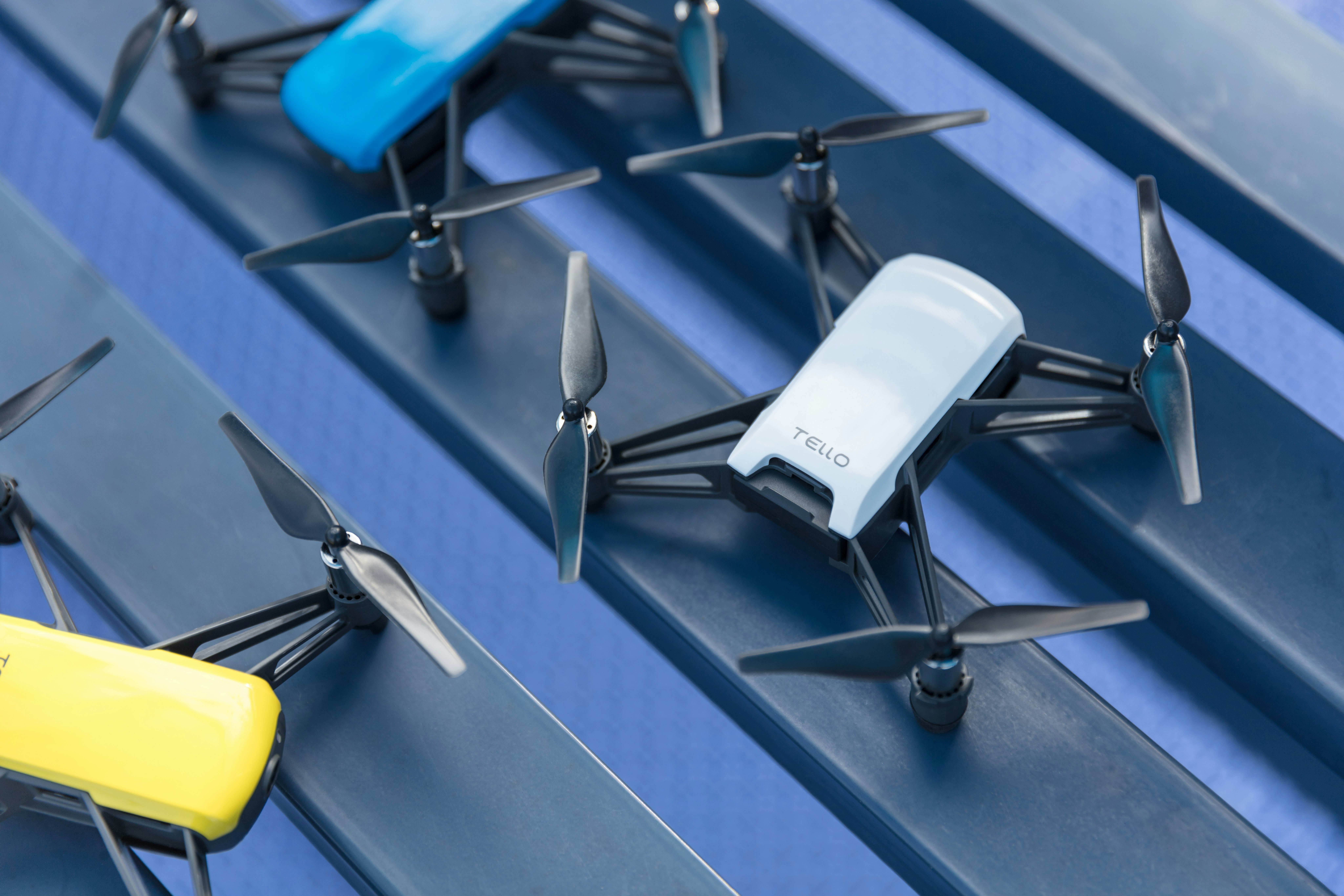 Three small drones in blue, white and yellow, with rotors extended