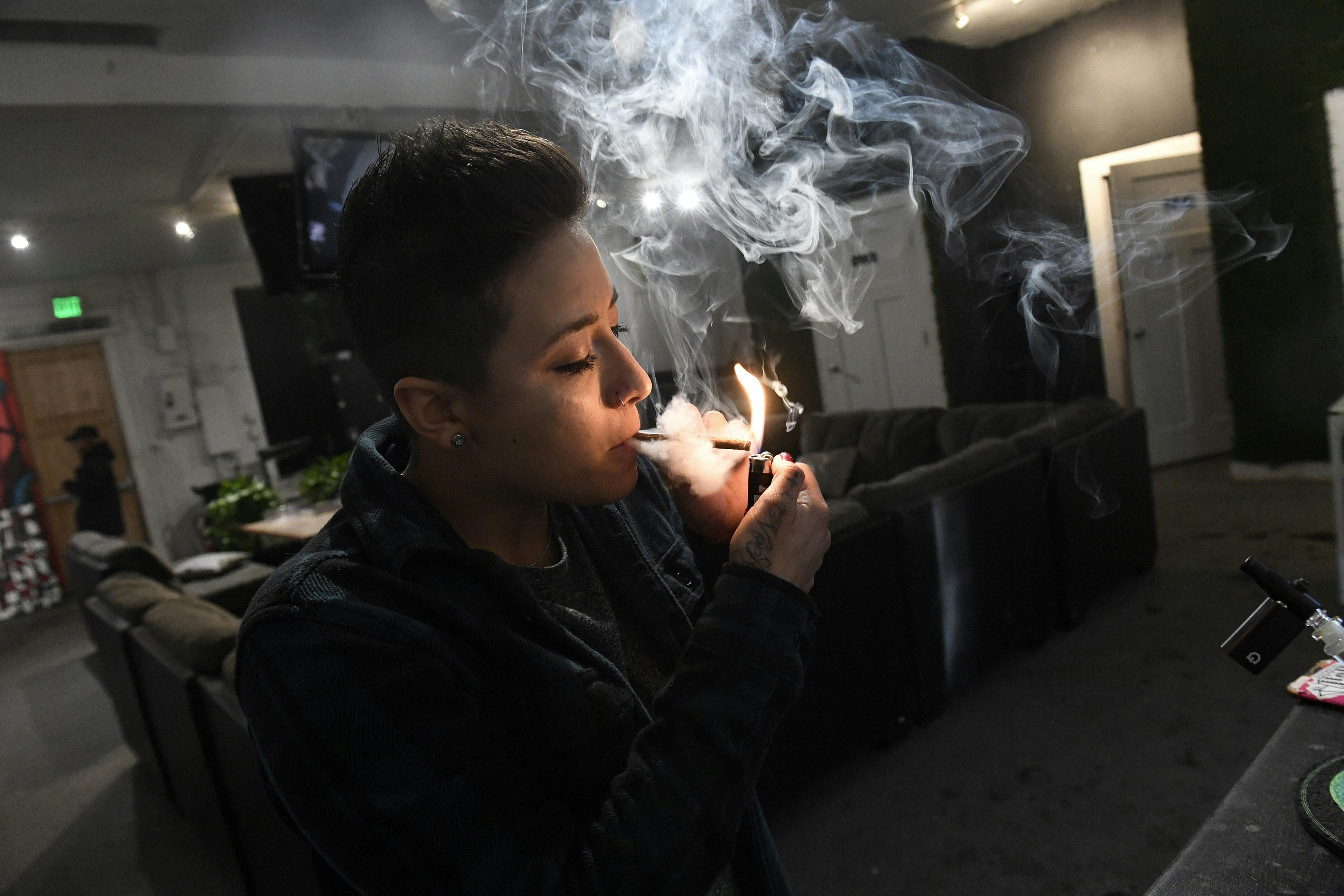 A manager at Tetra Private Lounge and Garden lights a joint. The flame illuminates her face and the wreath of white and grey smoke coming from the joint. Behind her is the comfortable, living-room like lounge area with big couches and doors leading to other parts of the club