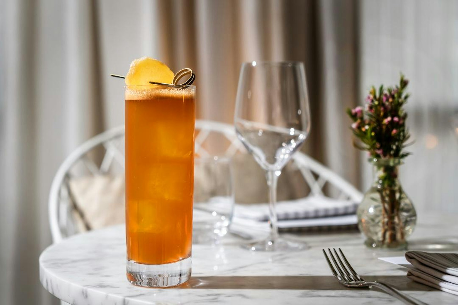 A tall class is filled with an orange-colored mocktail and sits on a round marble table.