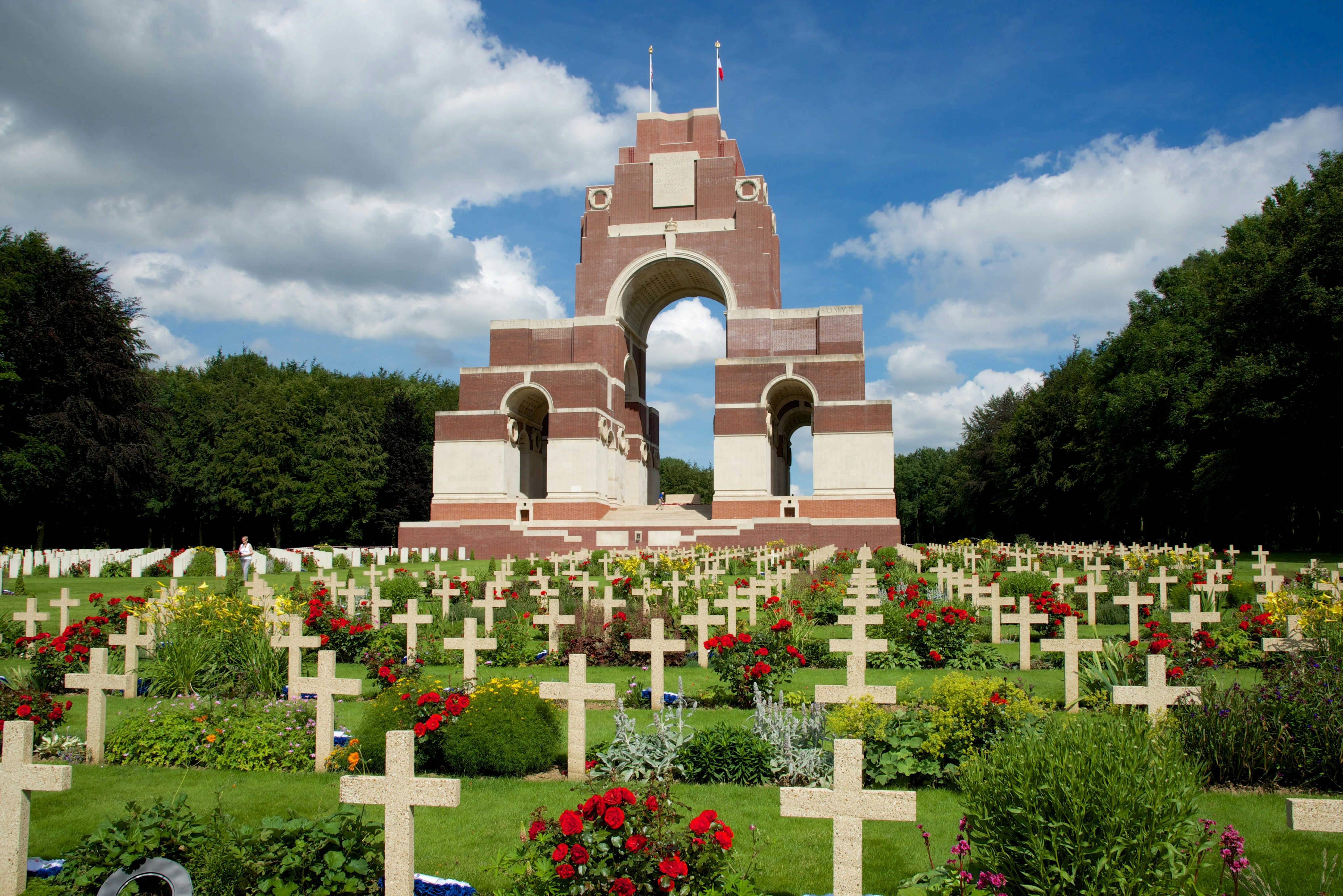 Thiepval Memorial in France; a memorial and burial site to some of those who died during the Battle of the Somme in the First World War. The monument is a large arched structure, while the surrounding laws are filled with poppies and small crosses acting as tombstones.