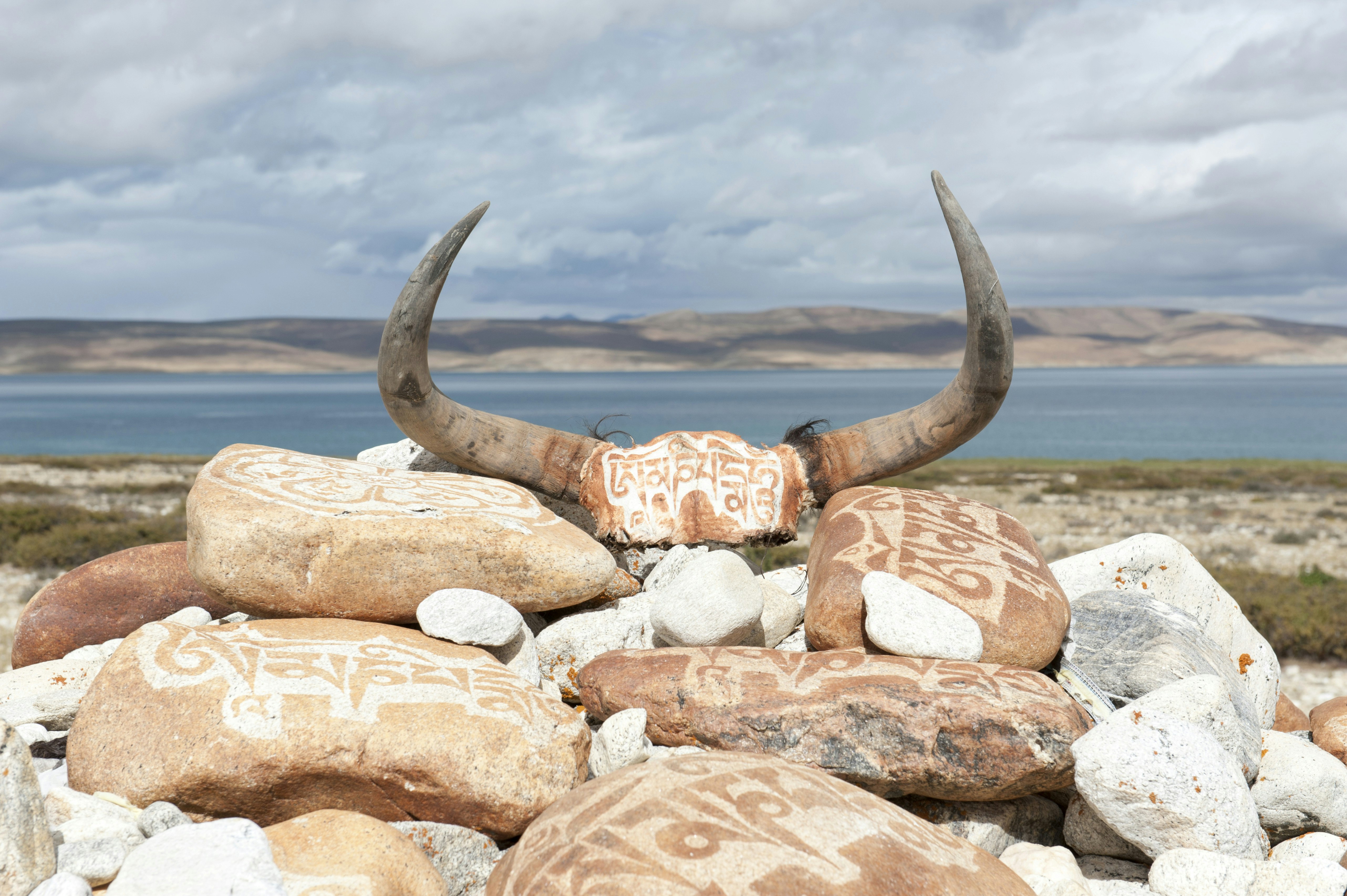 Yak horns and red stones covered in white Tibetan script are in a pile with the lake in the background.