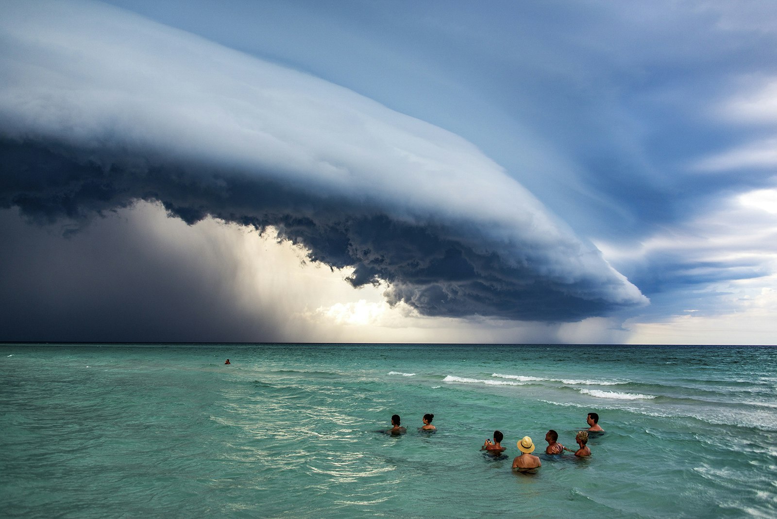 A picture of a group of people swimming in the sea while grey storm clouds gather above their heads
