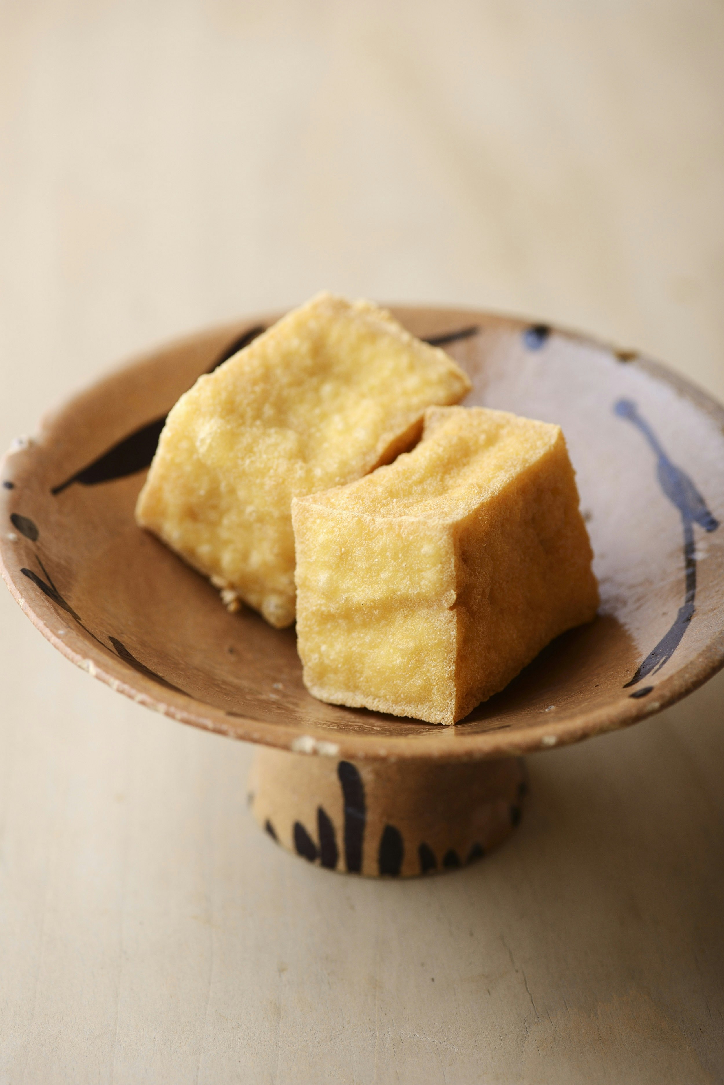 Two cubes of cooked tofu sit on a tiny elevated plate.