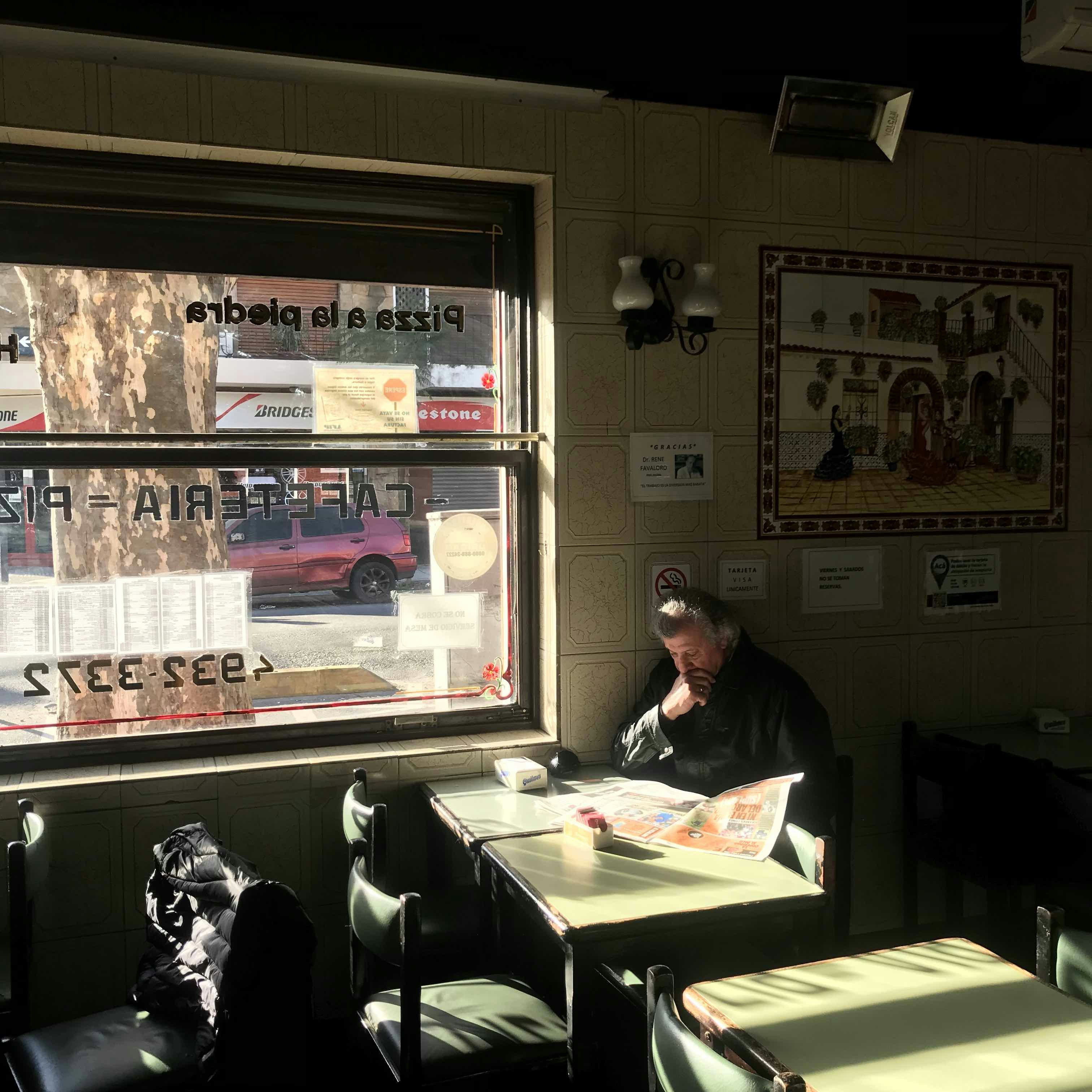 An elderly man sits by the window of a traditional cafe in Buenos Aires