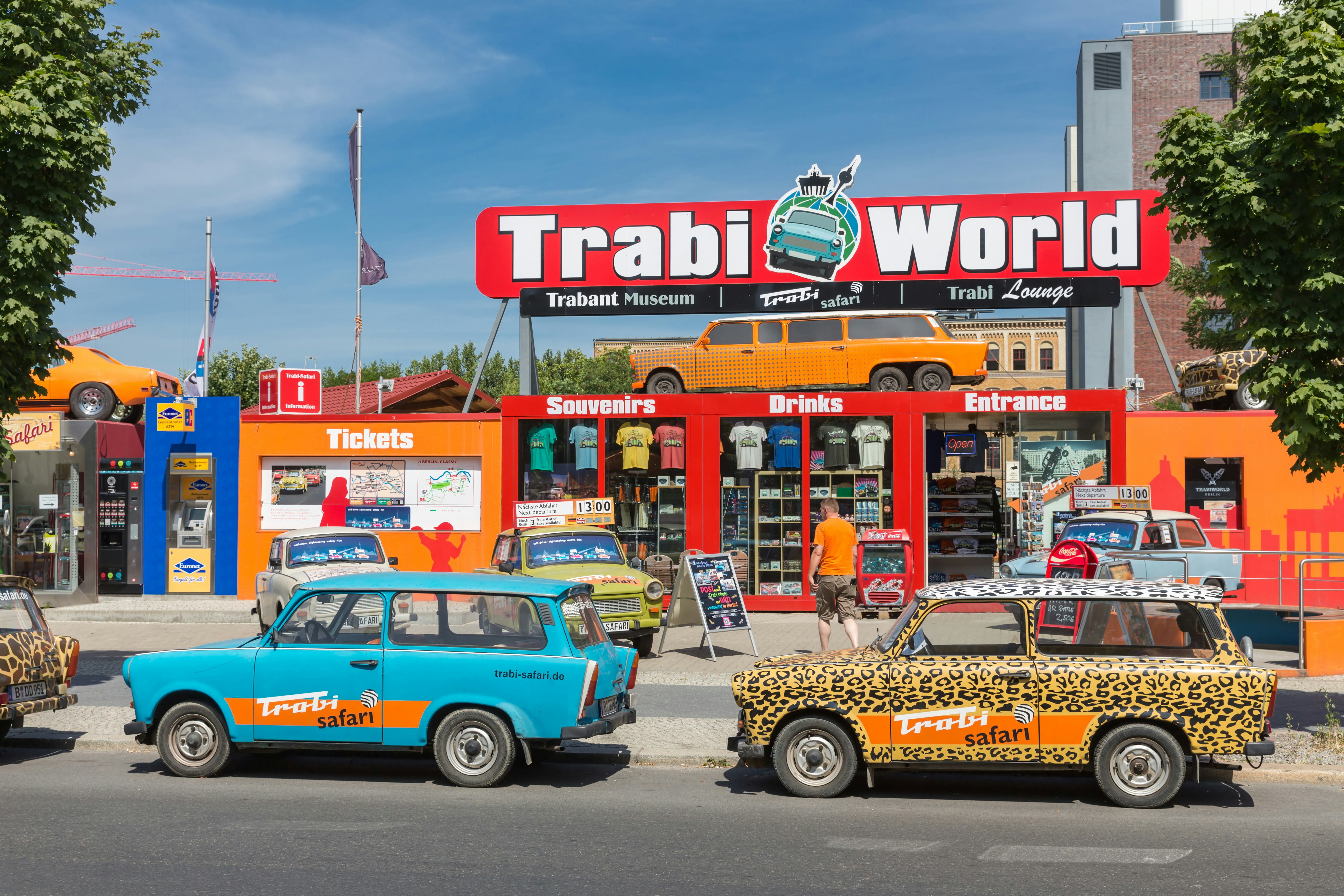 Colorful trabant cars parked on a street in front of a sign saying "Trabi World"