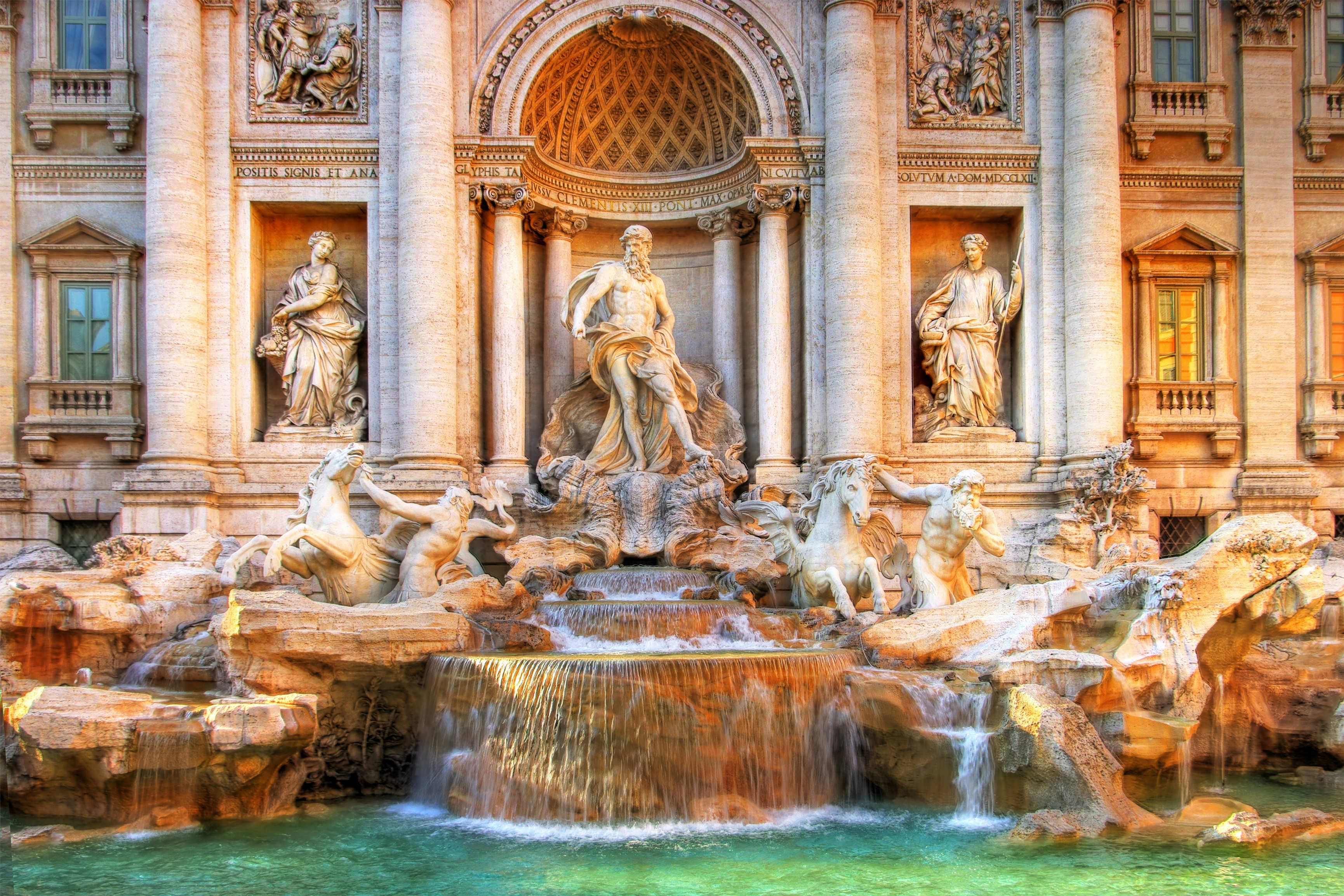 A frontal view of the Trevi fountain's marble statues in golden, warm light