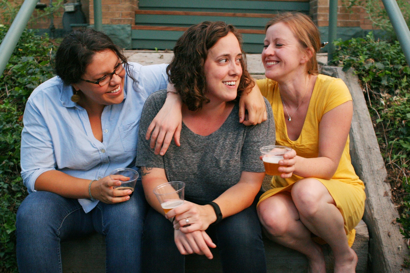 Three women sit on steps drinking beers