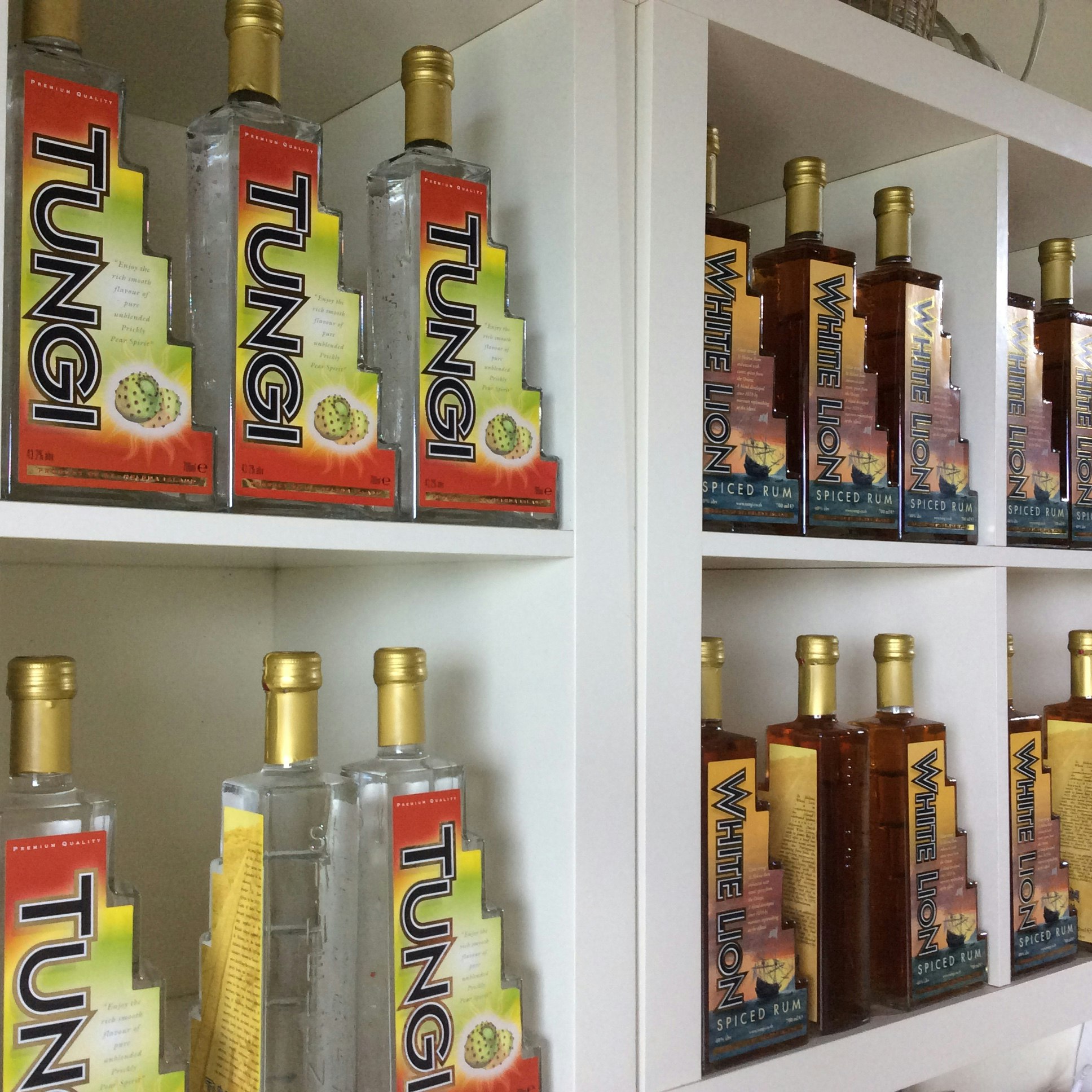 Step-shaded clear bottles of Tungi sit atop one another; next to these are identical shelves with brown step-shaped bottles of spiced rum.