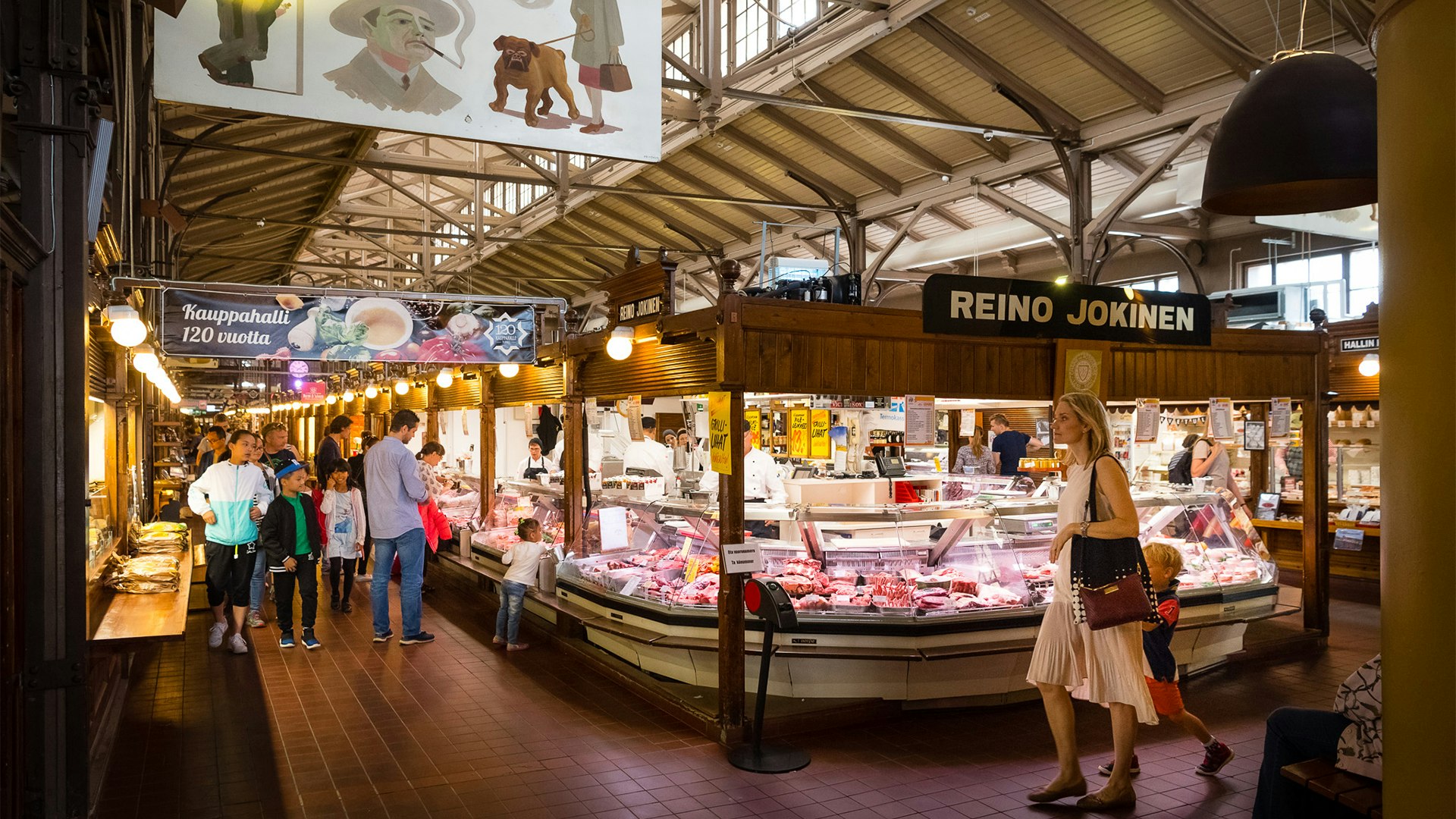 The interior of Turku Market Hall. Several vendors have stalls selling food in the vast space, and many shoppers are browsing.
