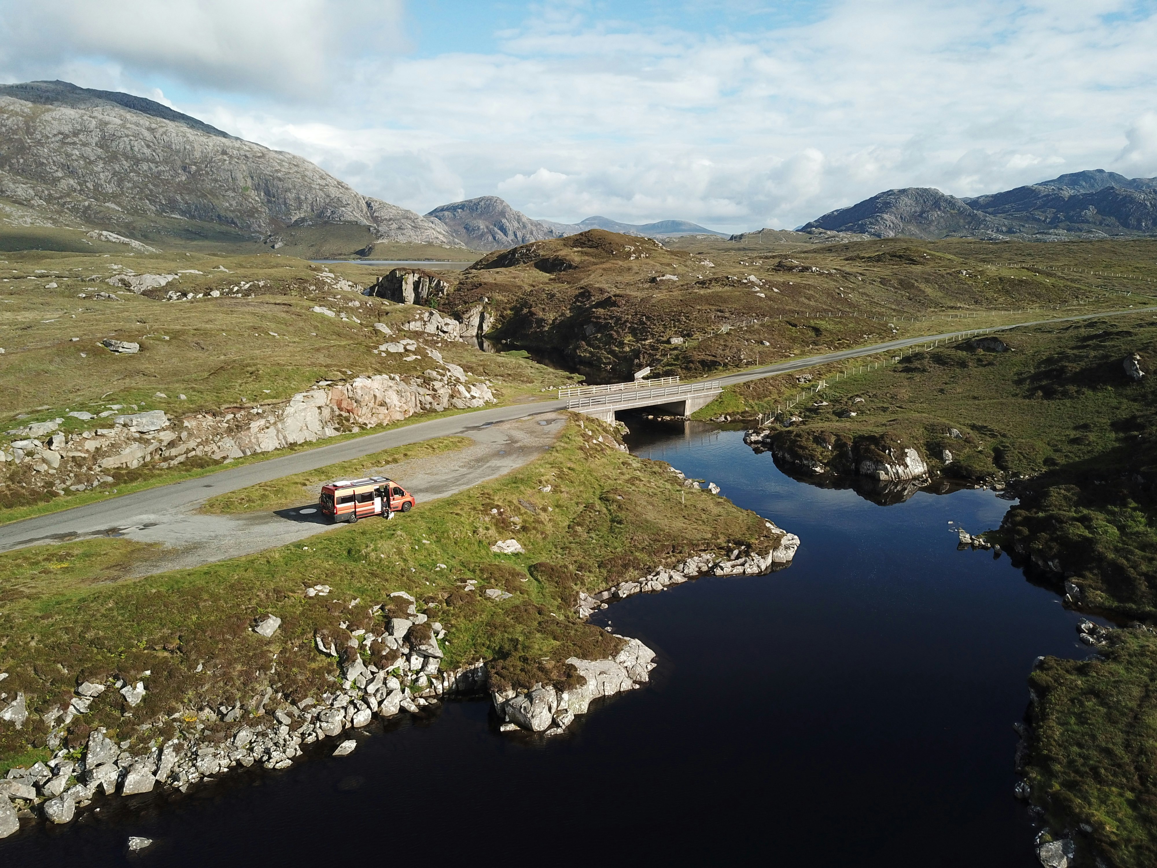 A drone image of Andrew with his van, parked up on a lay-by in Scotland. The van is parked on a patch of grass near the road, on the banks of a loch.