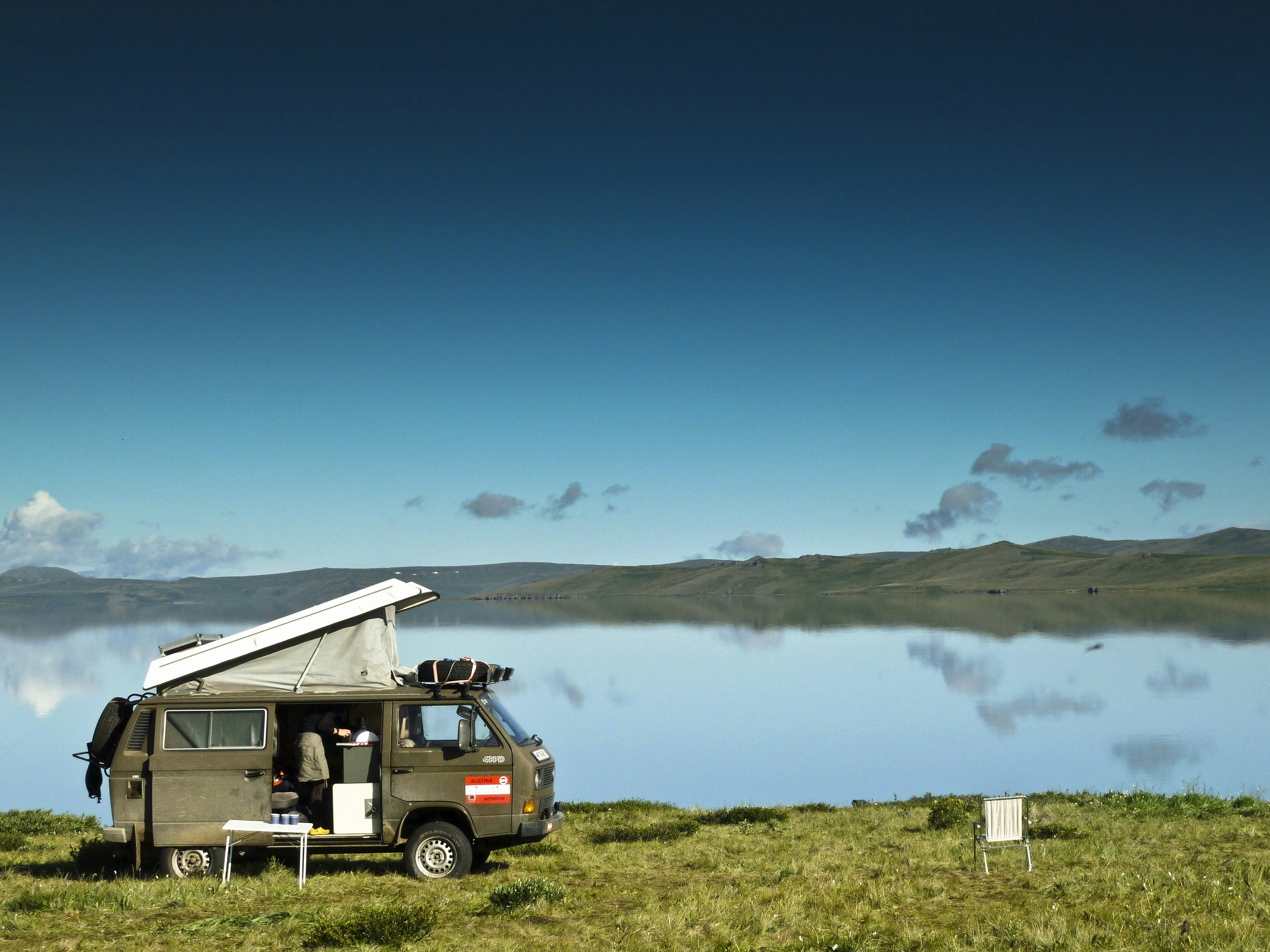 A van with its roof popped open is parked beside a vast lake