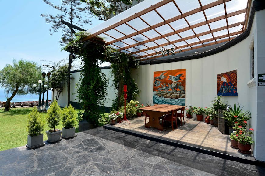 Веранда в Second Home Peru, доме скульптора Виктора Дельфина;  столовая украшена растениями в горшках, а на внешних стенах висят картины.