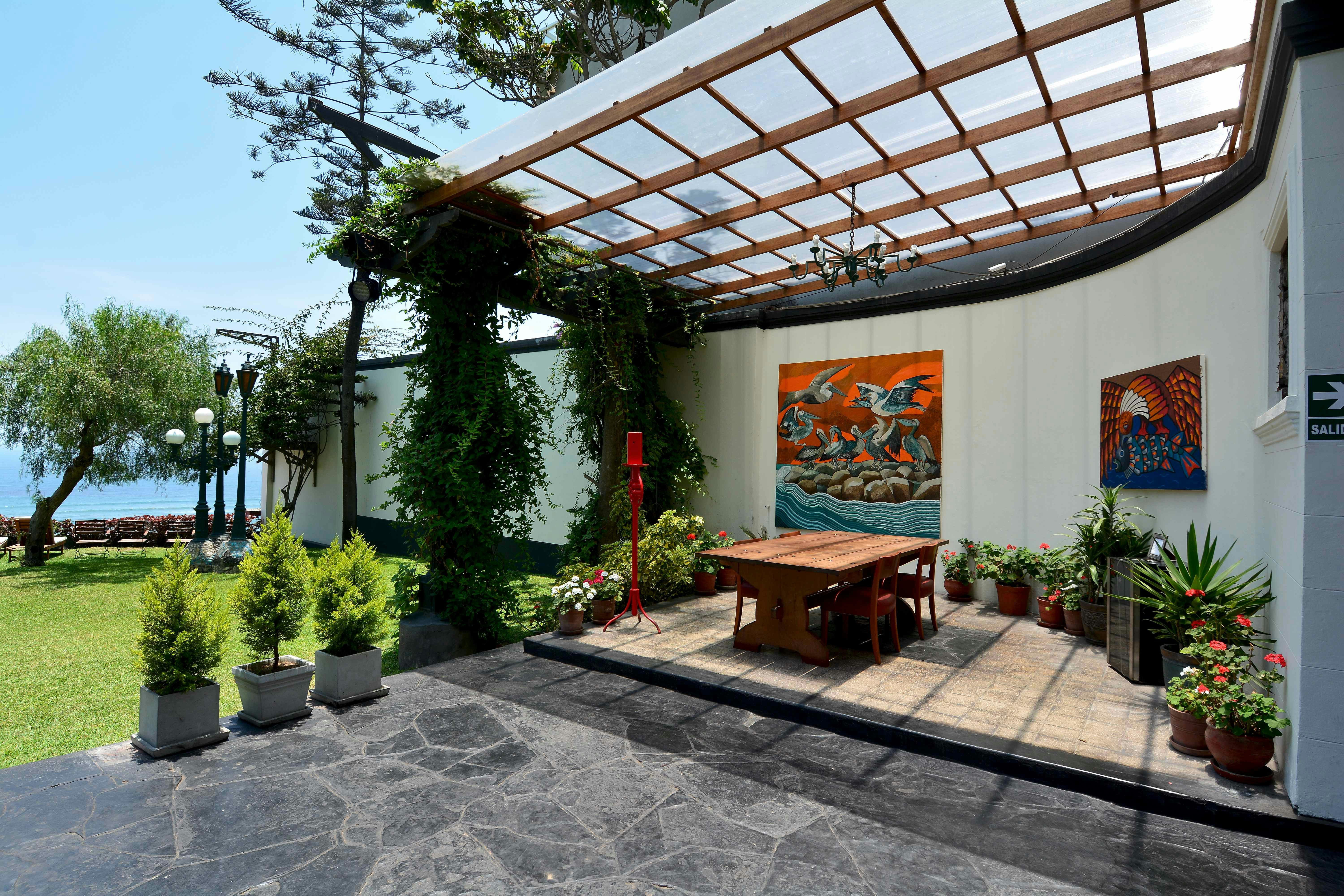 The veranda at Second Home Peru, the home of sculptor Víctor Delfín; a dining area is decorated with potted plants, and paintings hang on the exterior walls.