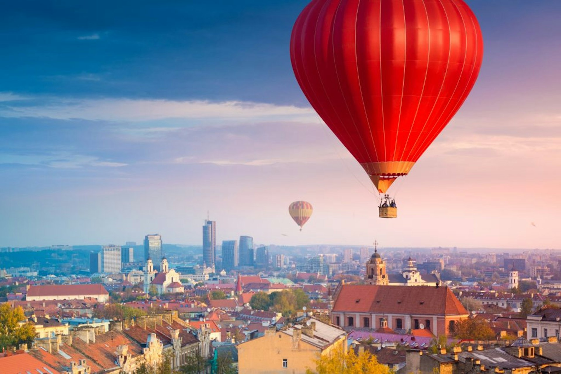 Hot air balloons flying over Vilnius during sunrise.