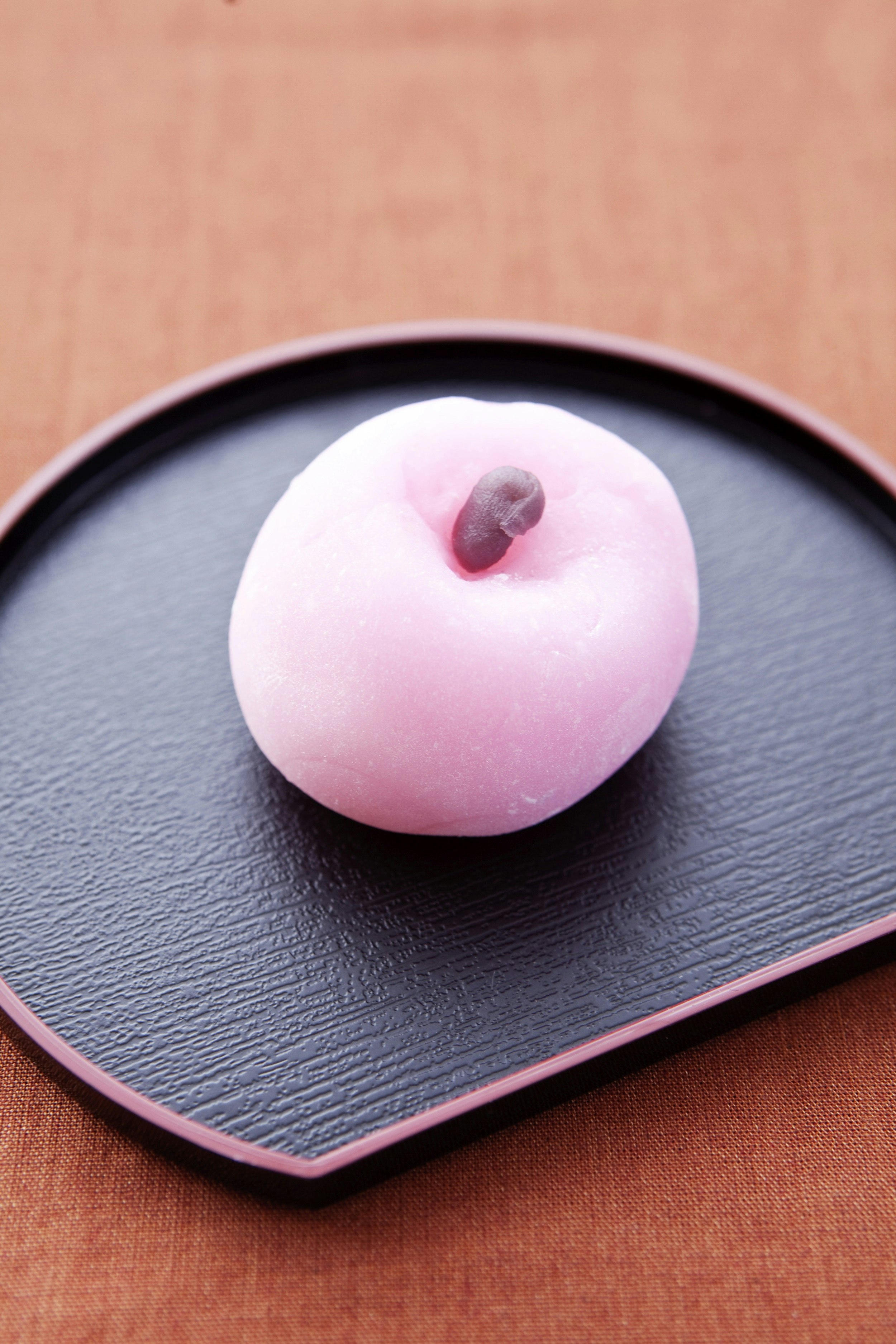 A light pink ball of a wagashi treat sits on a dark purple plate; inside it is a small purple sweet.