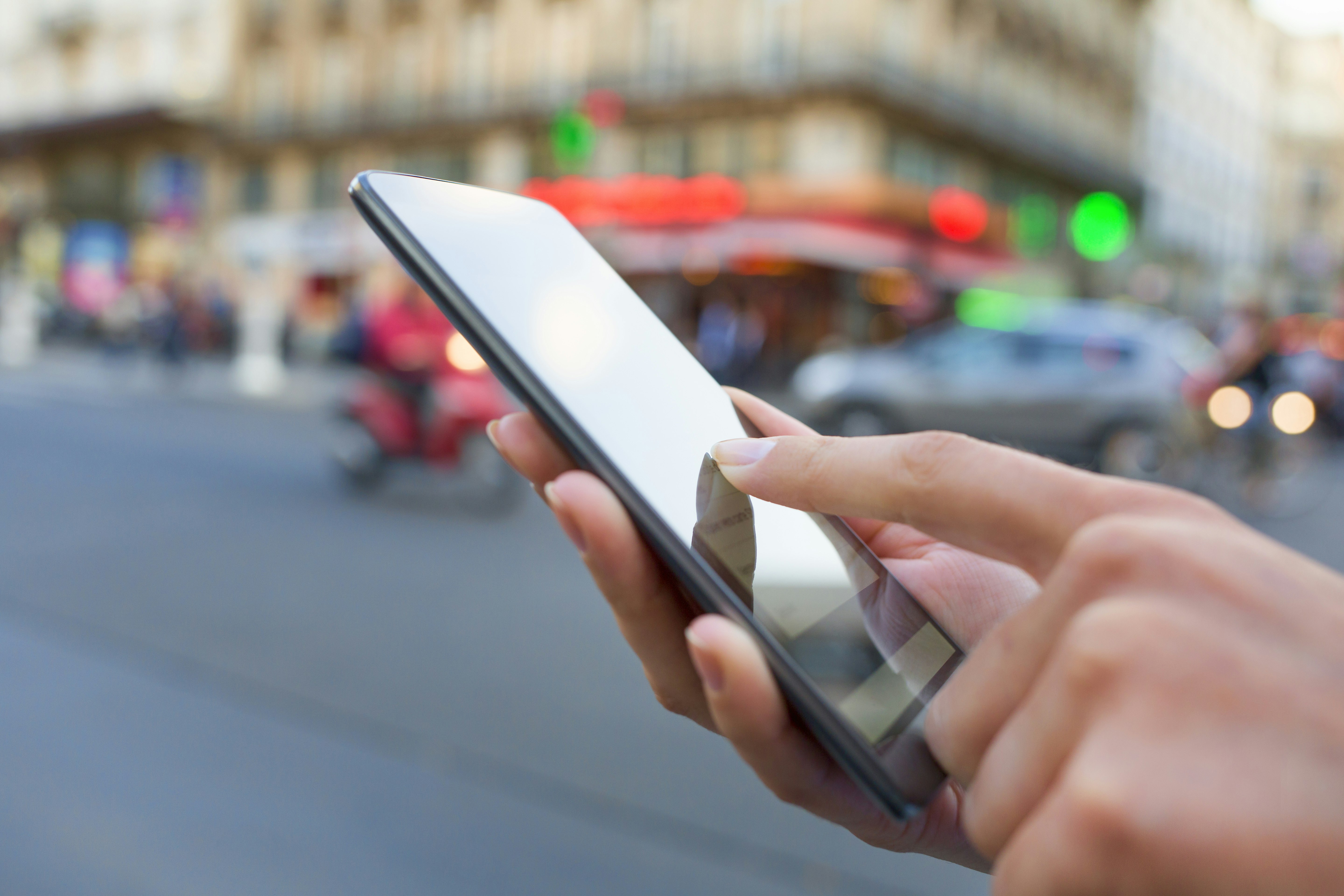 A woman uses her phone to book a rideshare on a city street