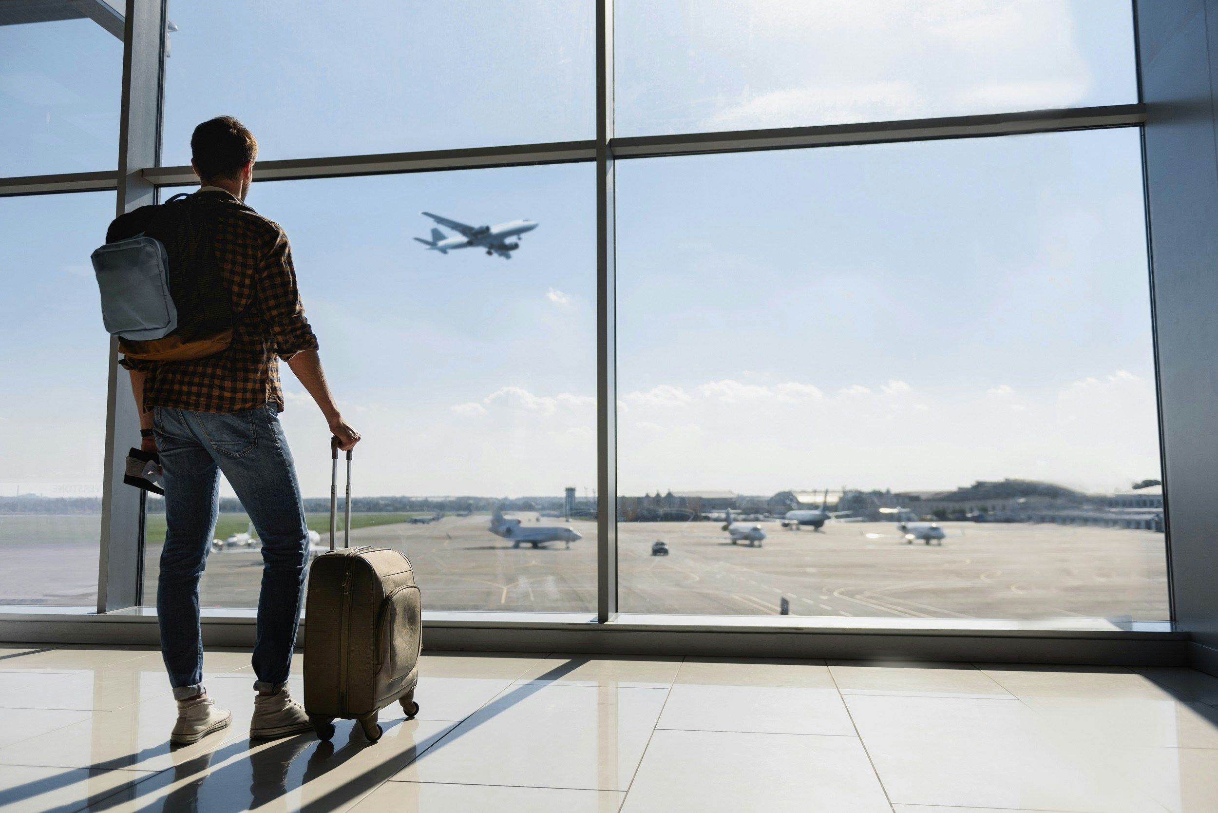 A man is standing in the airport watching a plane take off. 