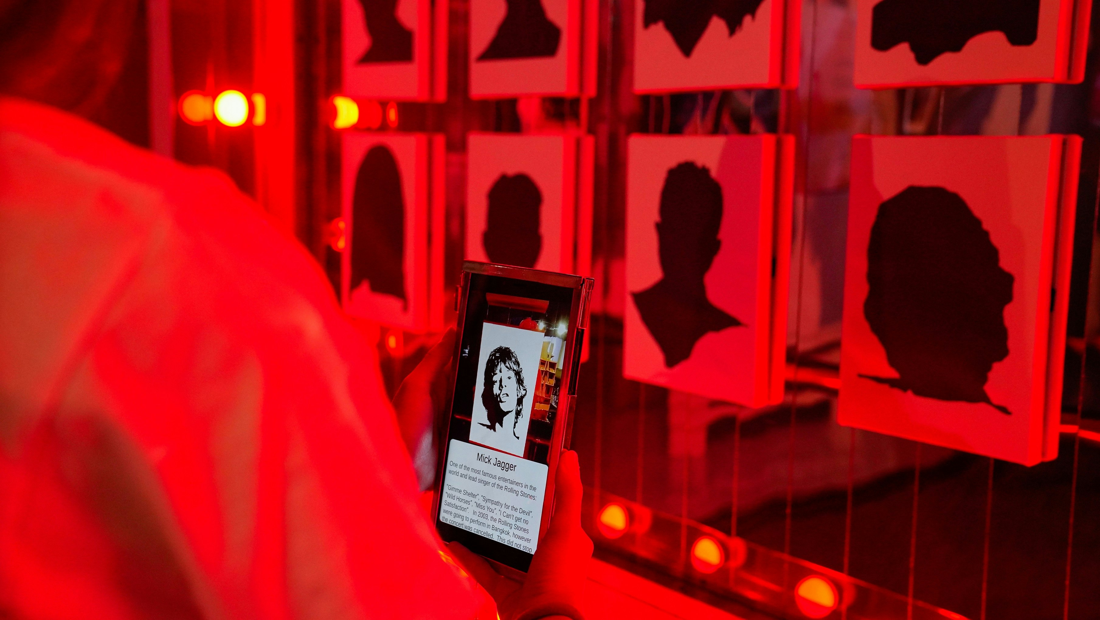 The wall of fame in the Patpong Museum. A visitor holds up a mobile phone to uncover who the silhouette on the wall belongs to. In this instance it is Mick Jagger.