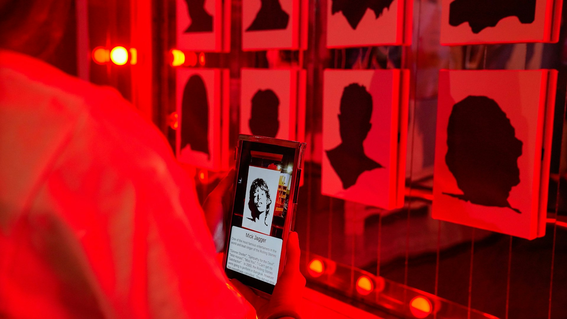 The wall of fame in the Patpong Museum. A visitor holds up a mobile phone to uncover who the silhouette on the wall belongs to. In this instance it is Mick Jagger.