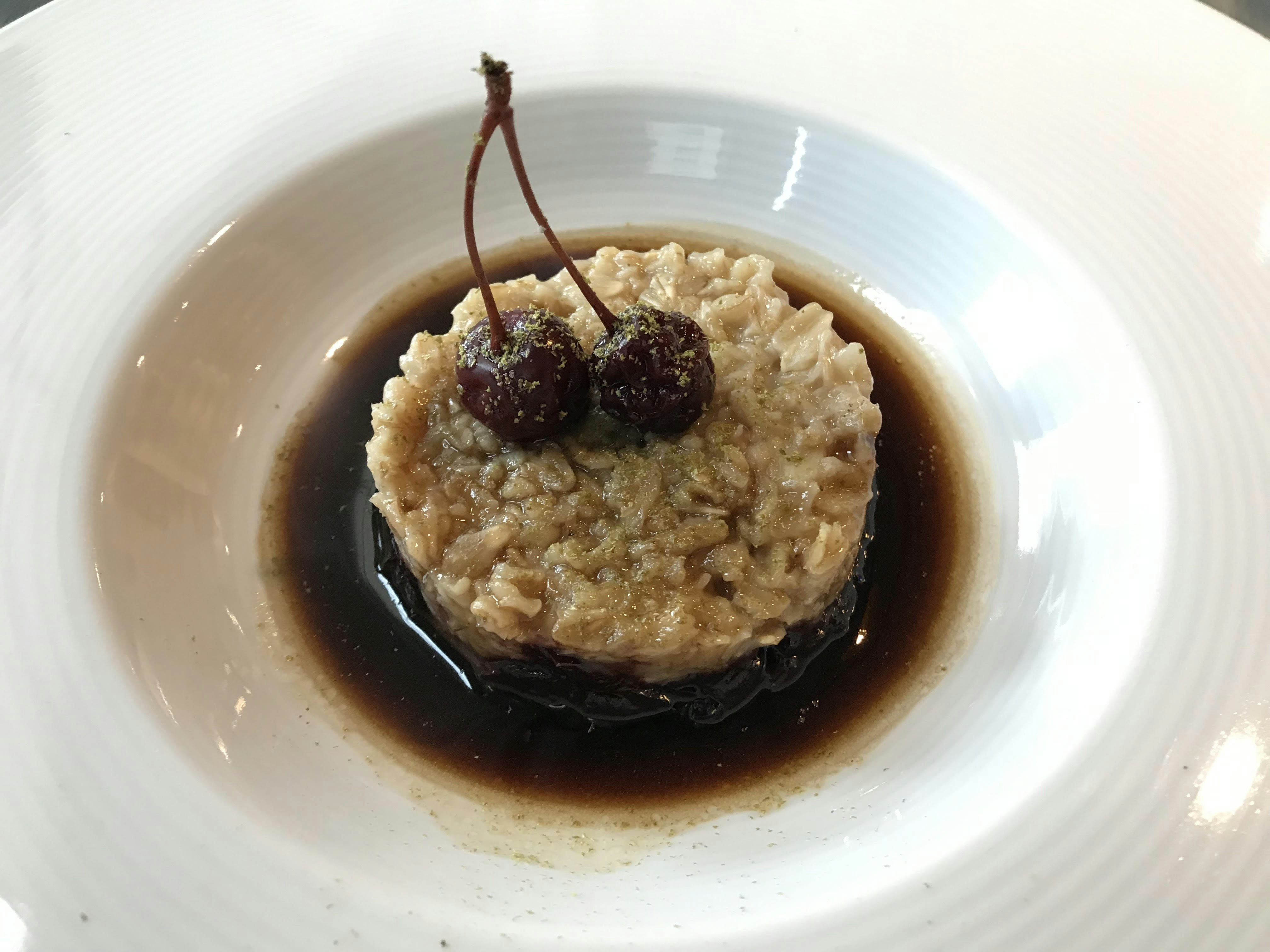 A bowl of dark soup with oatmeal and cherries.