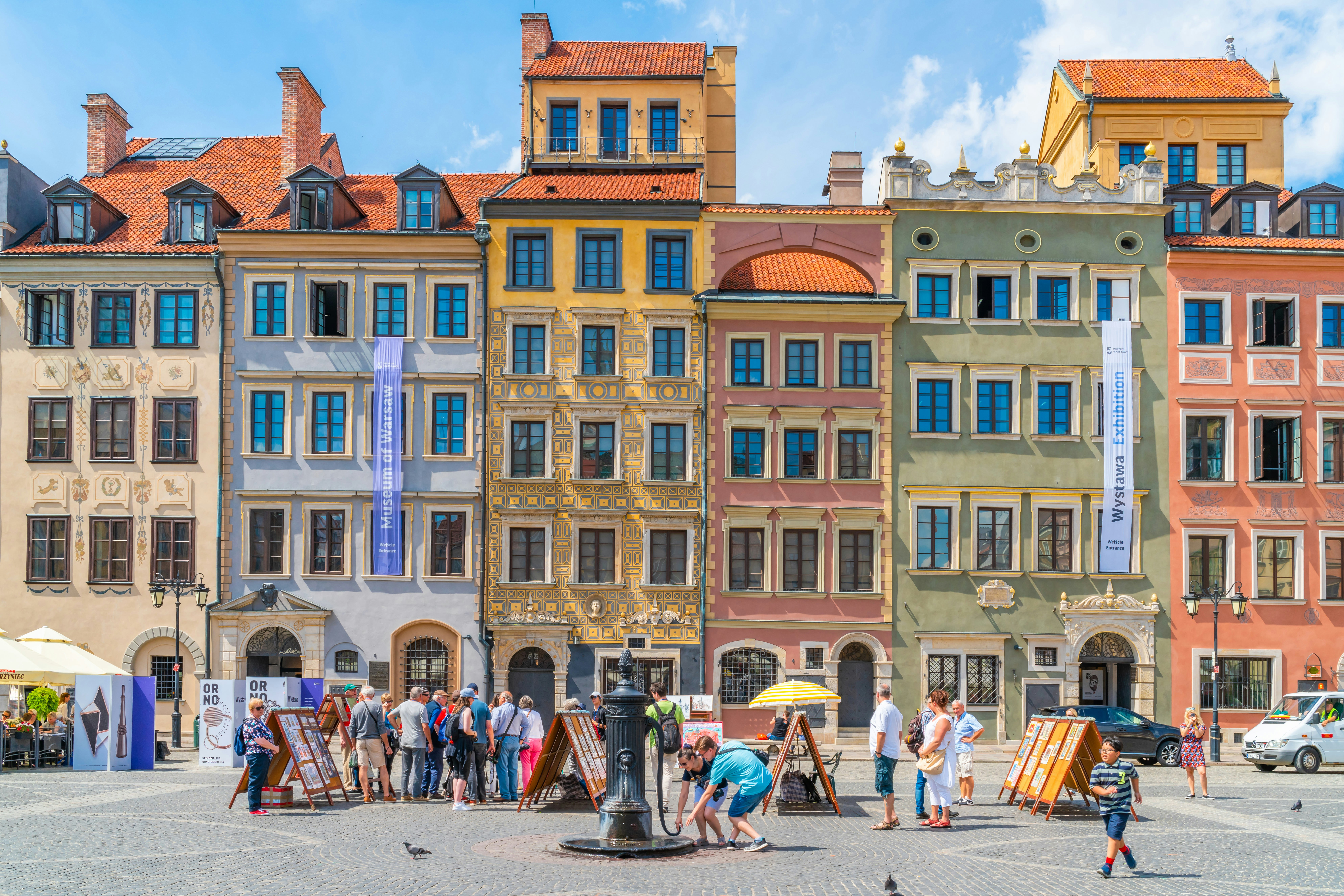 Crowds of people enjoy a sunny day in front of the colourful buildings of Warsaw. 
