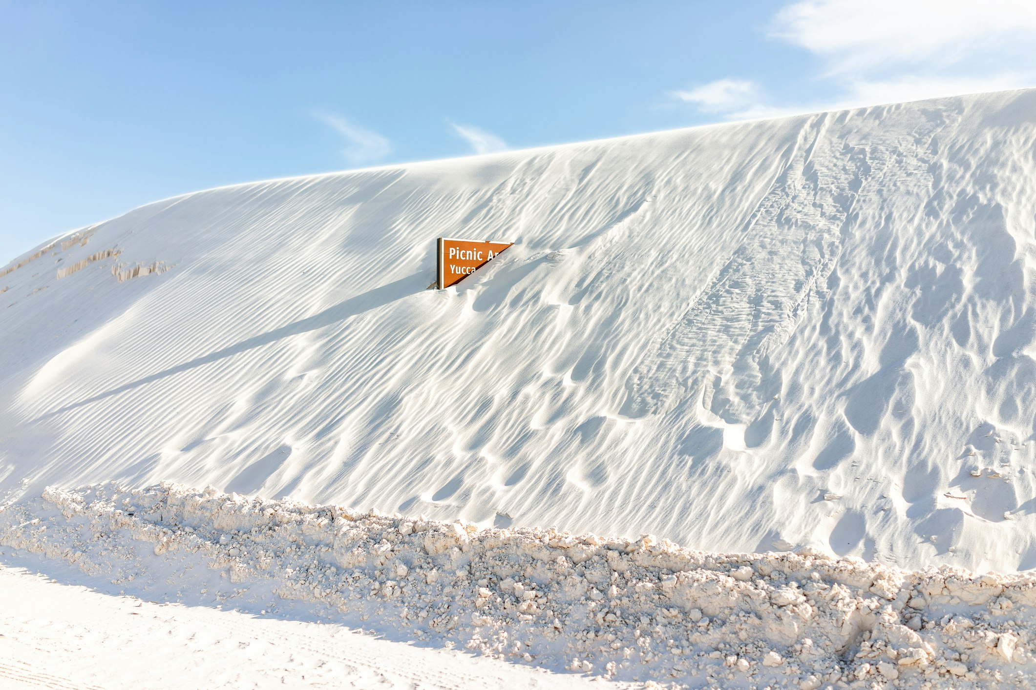 A brown park sign indicating the Yucca Picnic Area is half-buried in a sugary sand dune at White Sands National Park in New Mexico