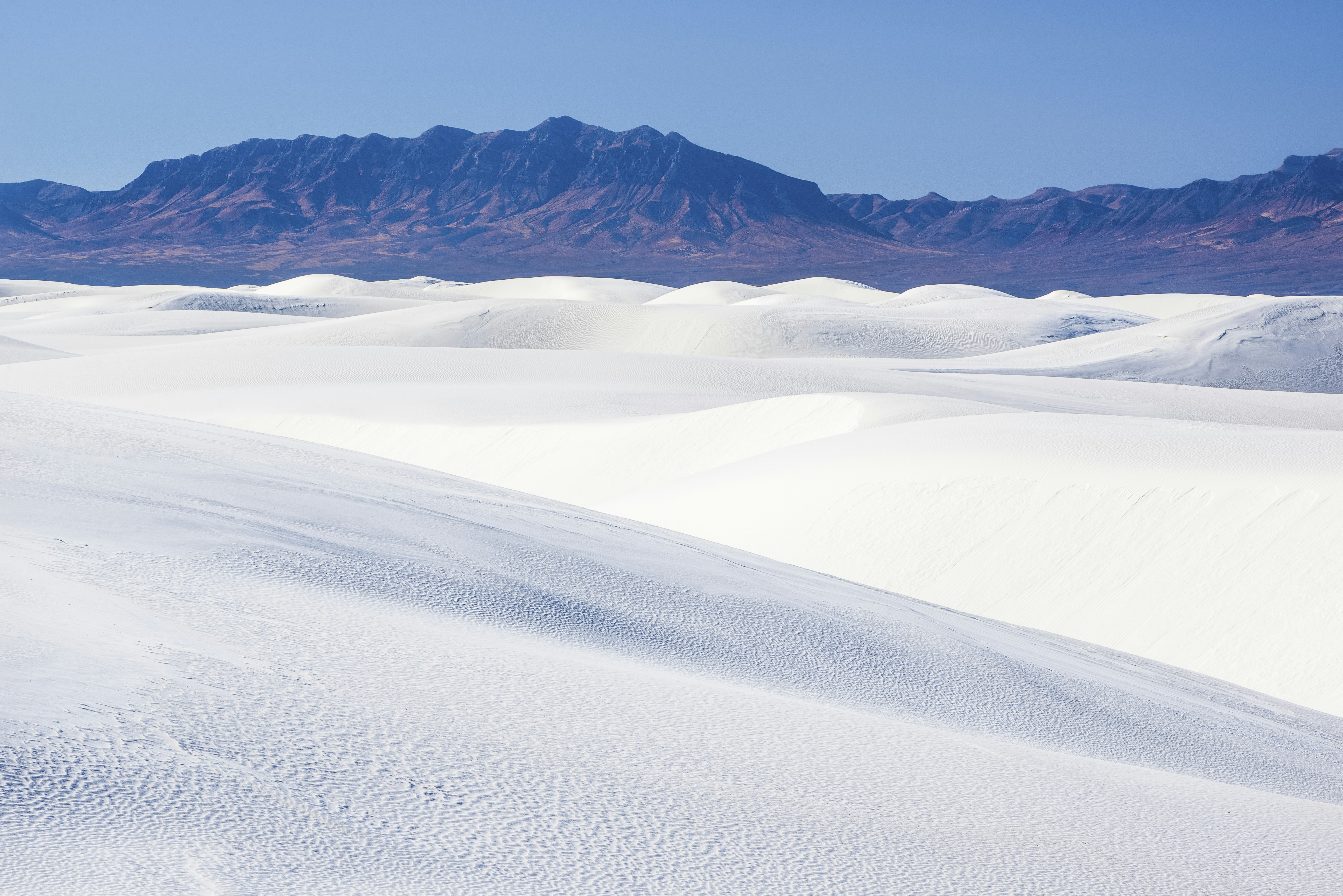 The white gypsum sand dunes spread out like powdered sugar in front of the blue and red San Andres Mountains in White Sands National Park in southern New Mexico
